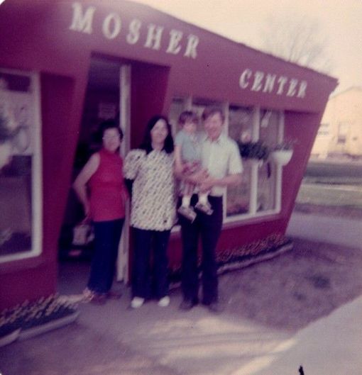 Three people standing outside a maroon Moser Center building, with one holding a child.