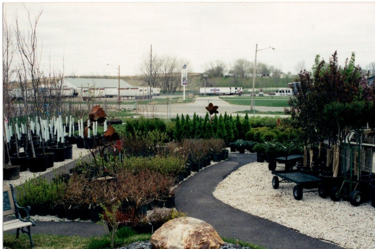 Garden center with potted plants, a curving gravel path, and a worker in the background