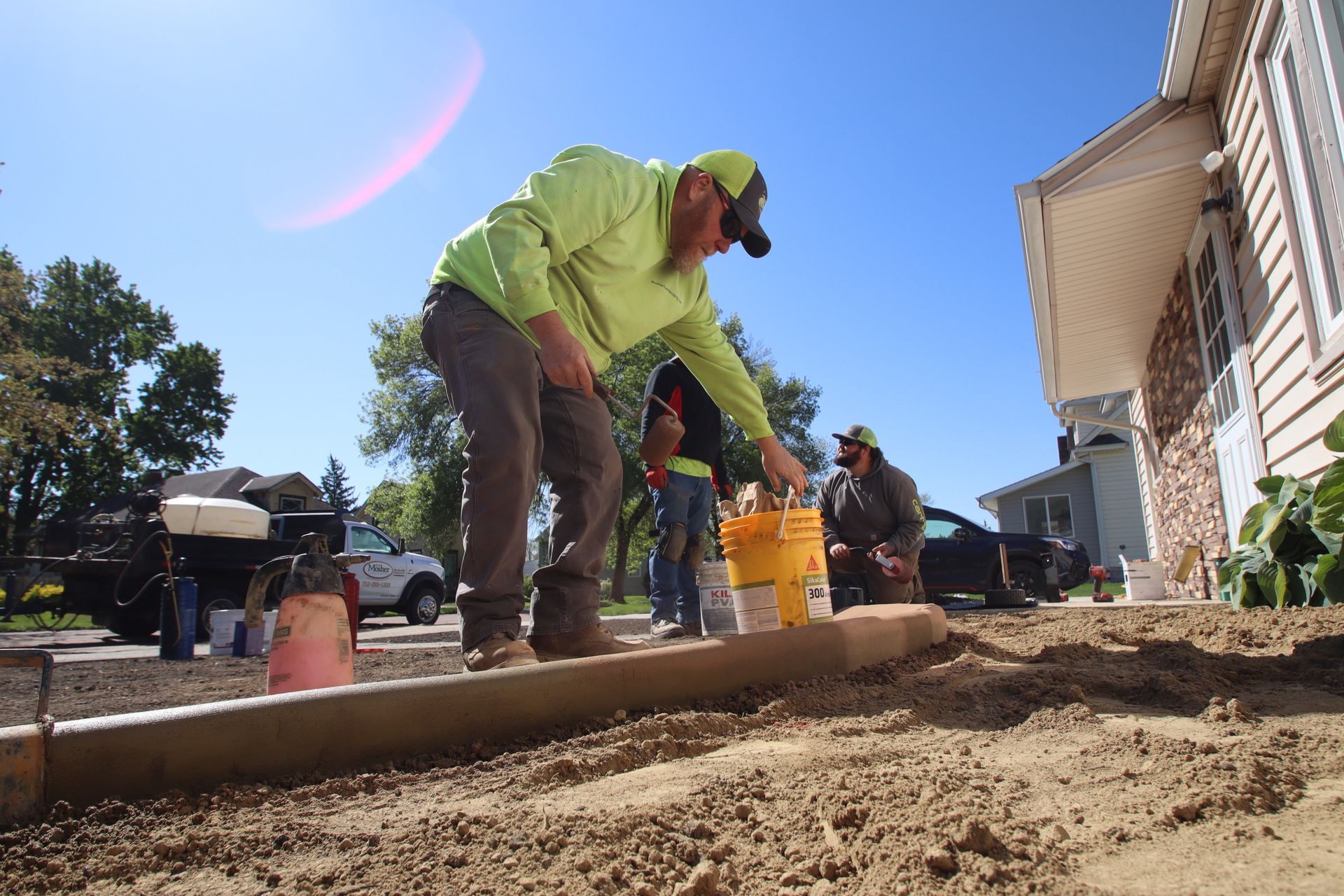 Worker in a neon green jacket pours material at a house foundation on a sunny day.
