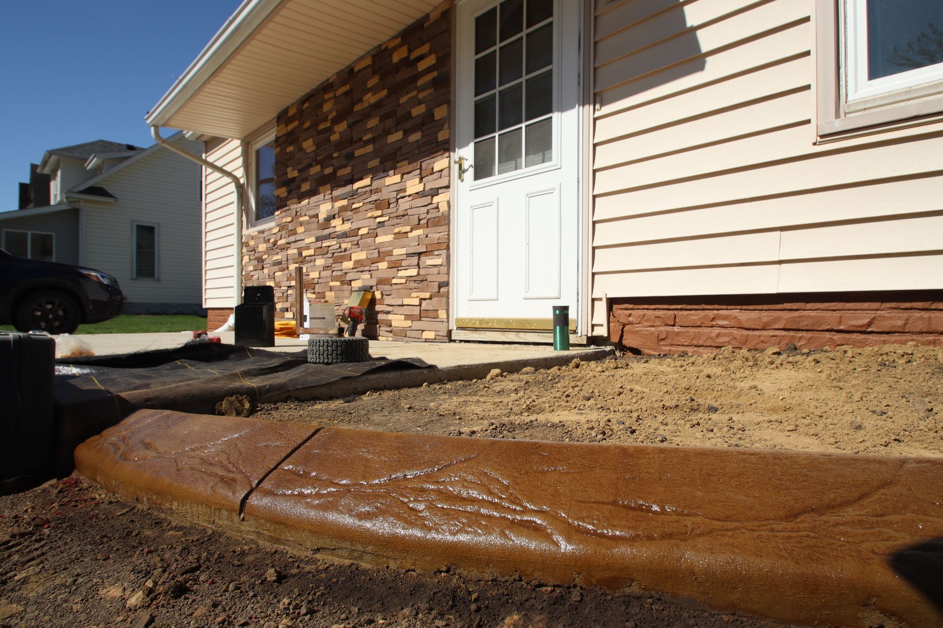 House exterior with fresh concrete walkway and curb near a front door, in bright sunlight