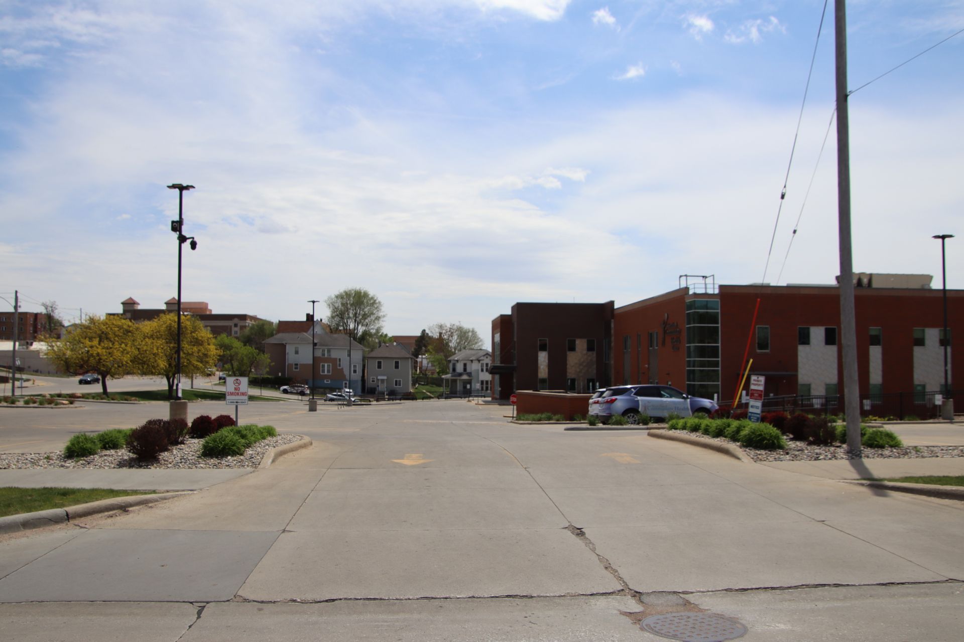 Quiet small-town street with brick buildings, parked cars, and a wide concrete road under a blue sky.