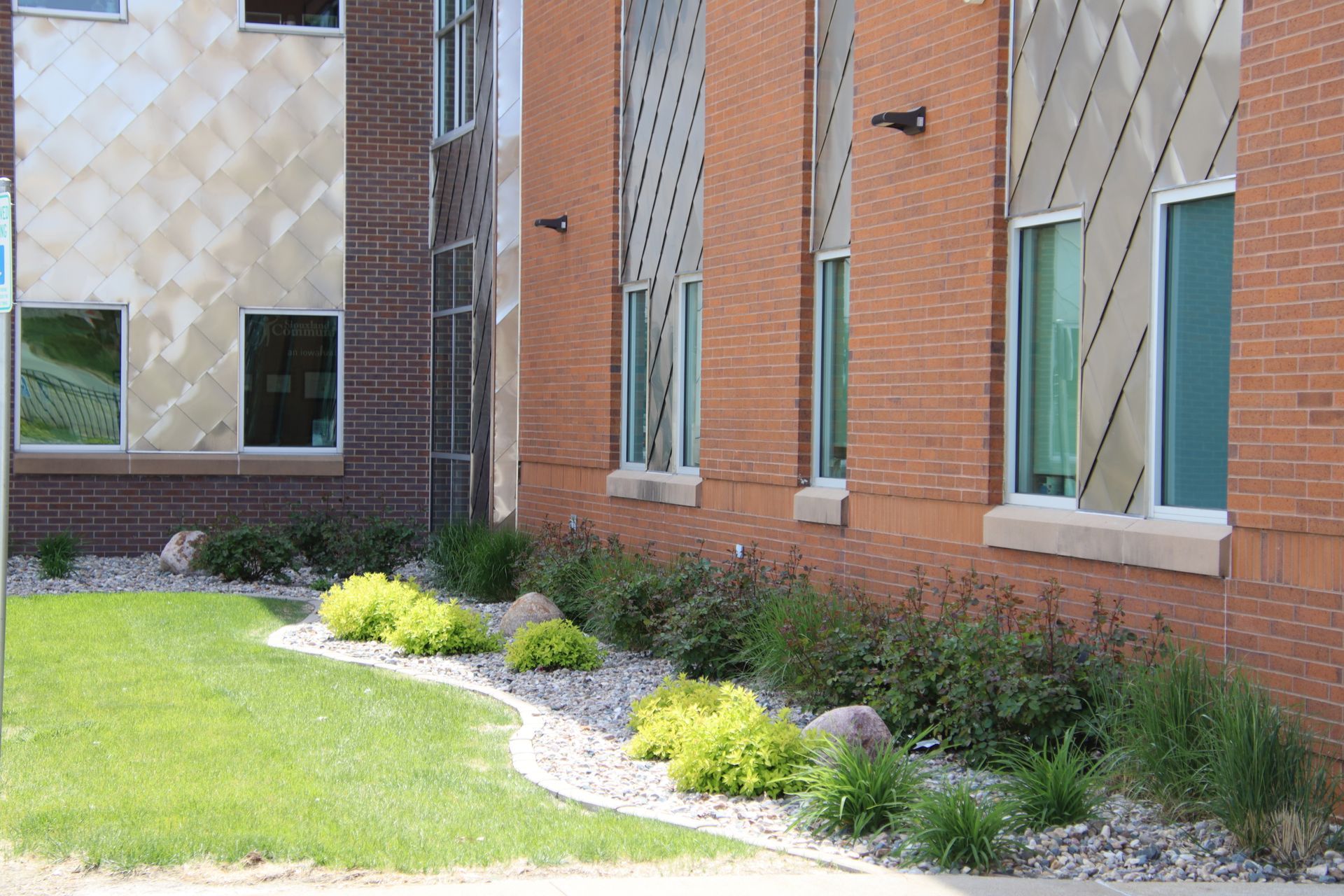 Brick building exterior with windows and a landscaped green lawn and shrubs