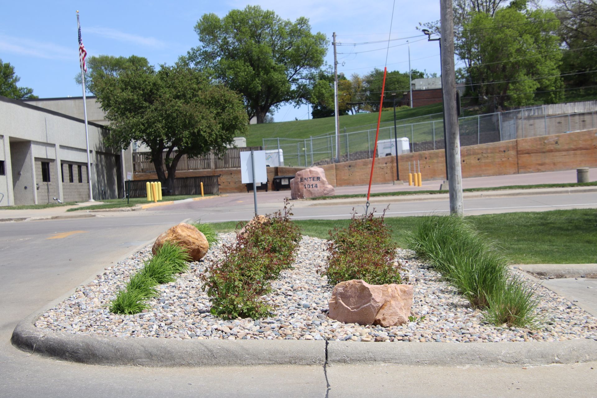 Small roadside landscaped median with gravel, rocks, and young plants near an intersection