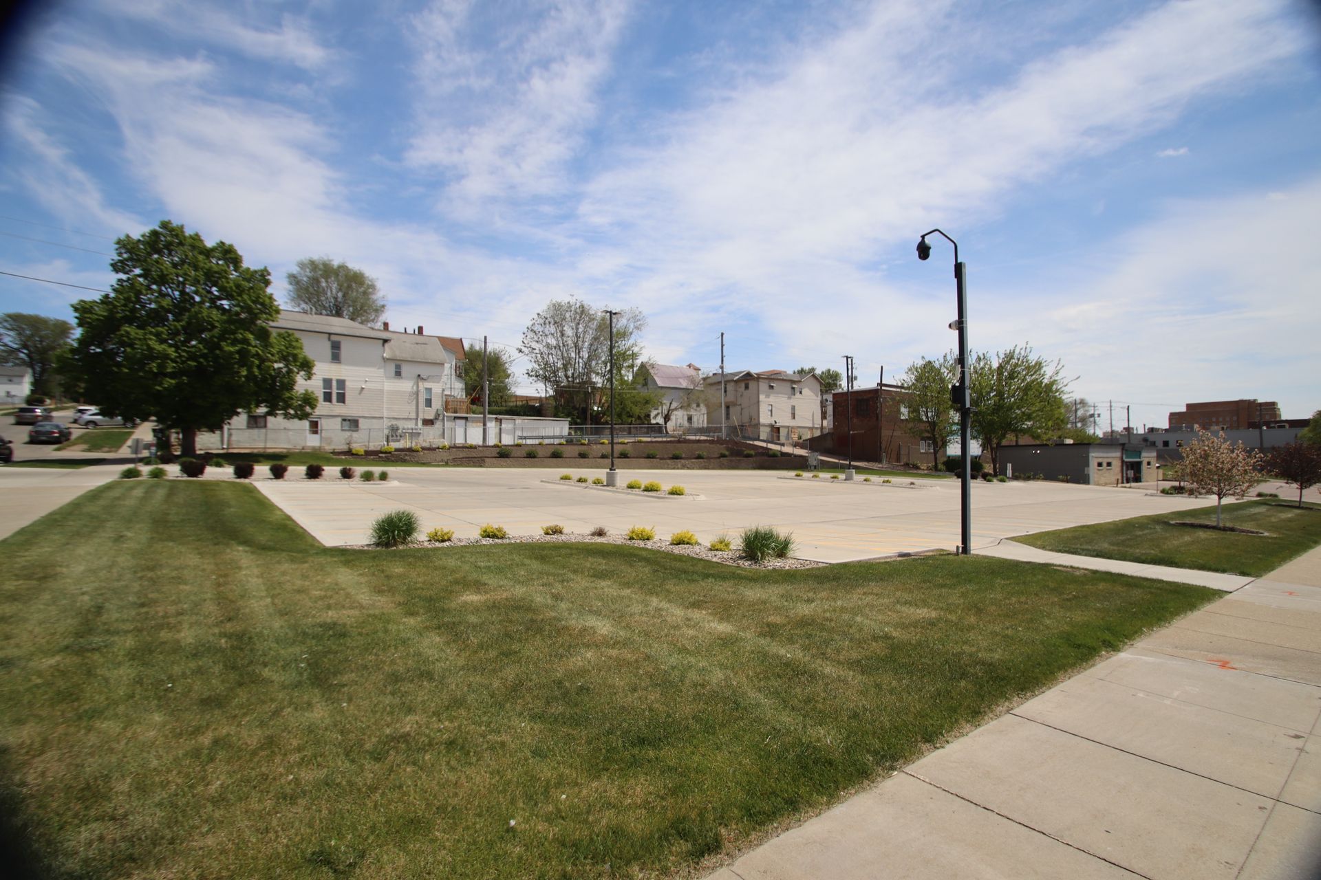 Empty suburban park with grass, sidewalks, a lamp post, and houses under a cloudy sky