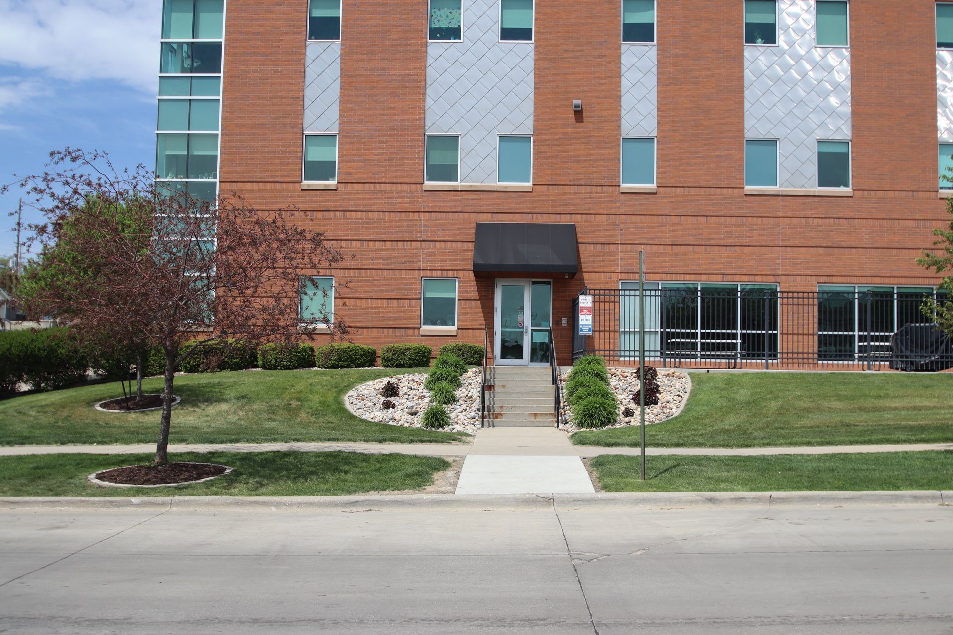 Brick apartment building with central entrance, windows, lawn, and sidewalk in front