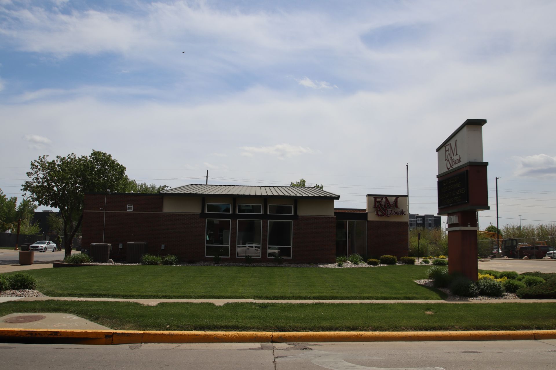 Brick building with a green lawn and sign by the road under a cloudy sky