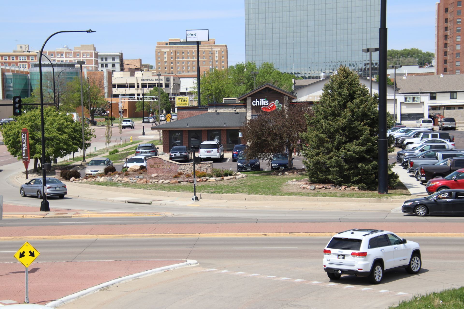 Downtown street scene with cars, a small building, and a large glass office tower in the background