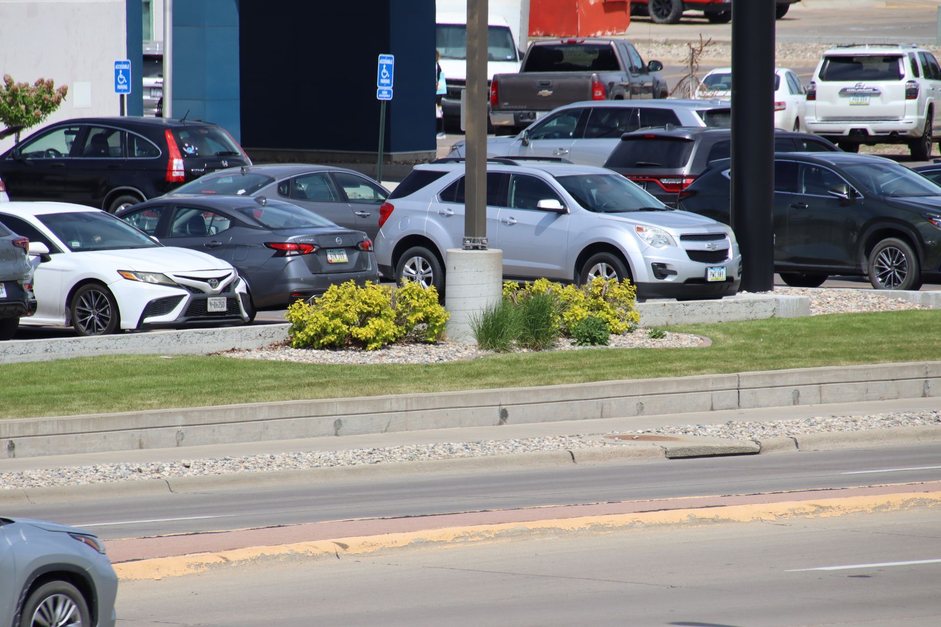Parked cars in a lot beside a road, with a white lamp post and building in the background