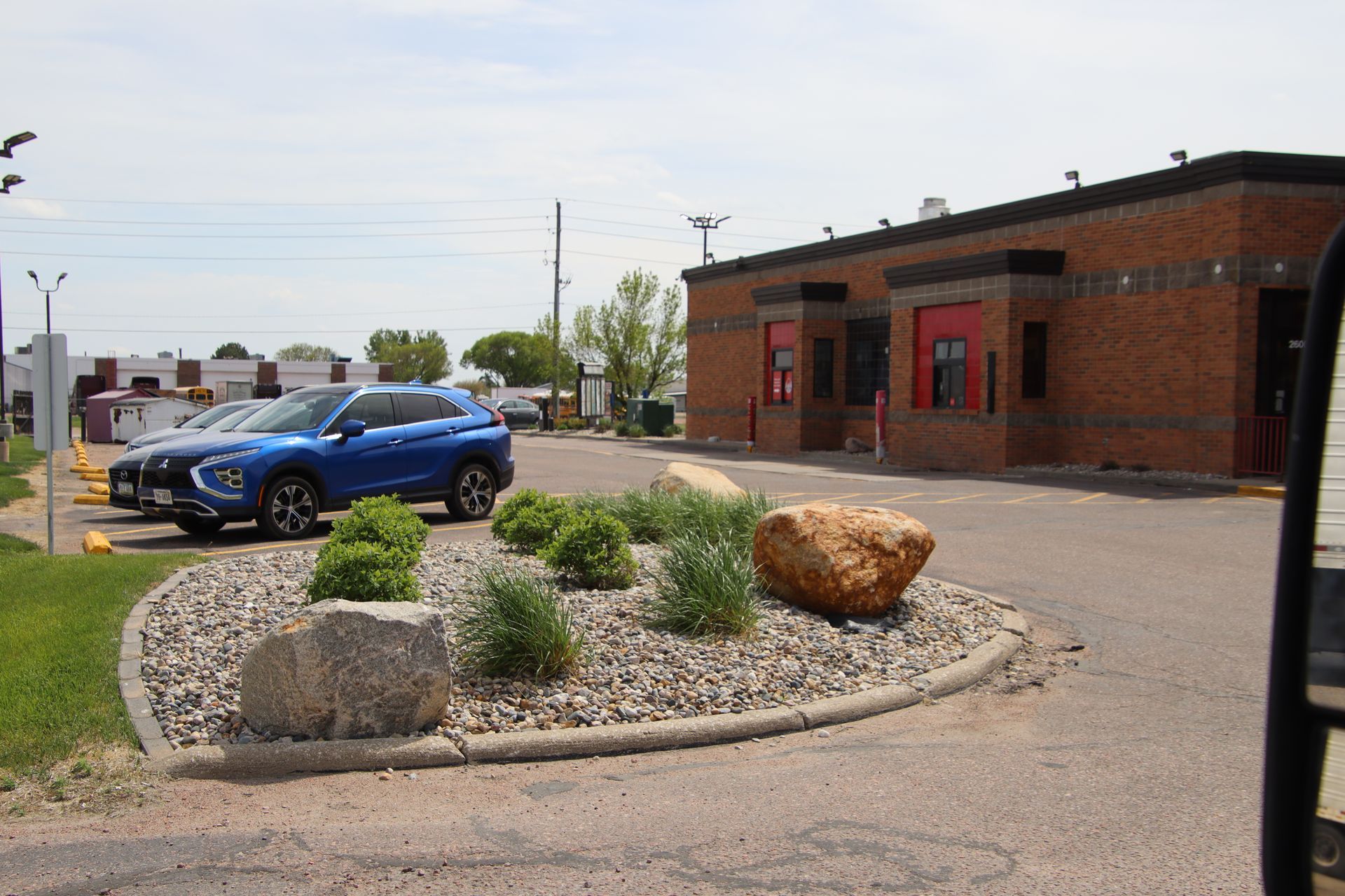 Blue SUV parked beside a brick building and landscaped gravel island with rocks and shrubs