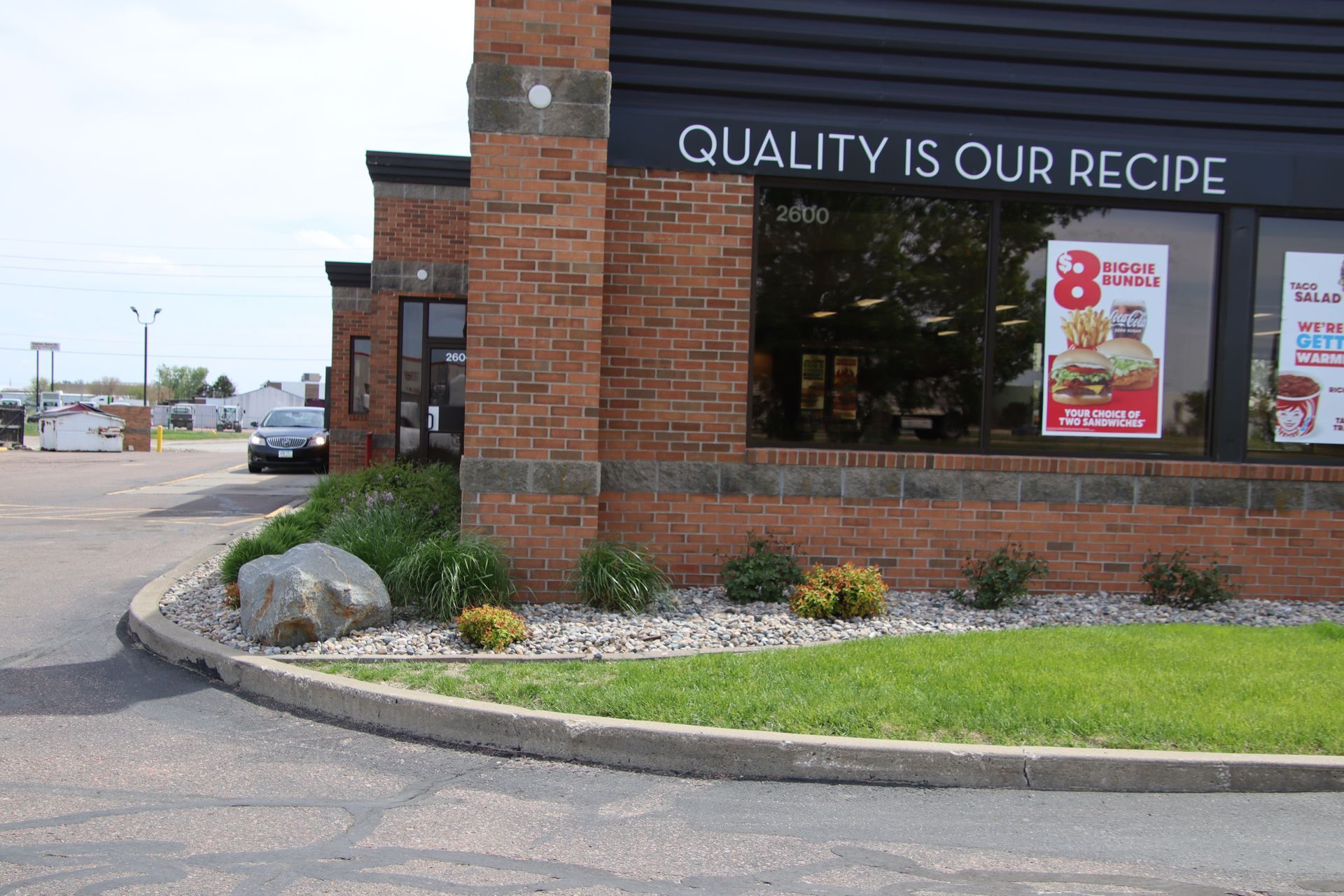 Brick fast-food restaurant corner with “Quality Is Our Recipe” sign and drive-thru window.