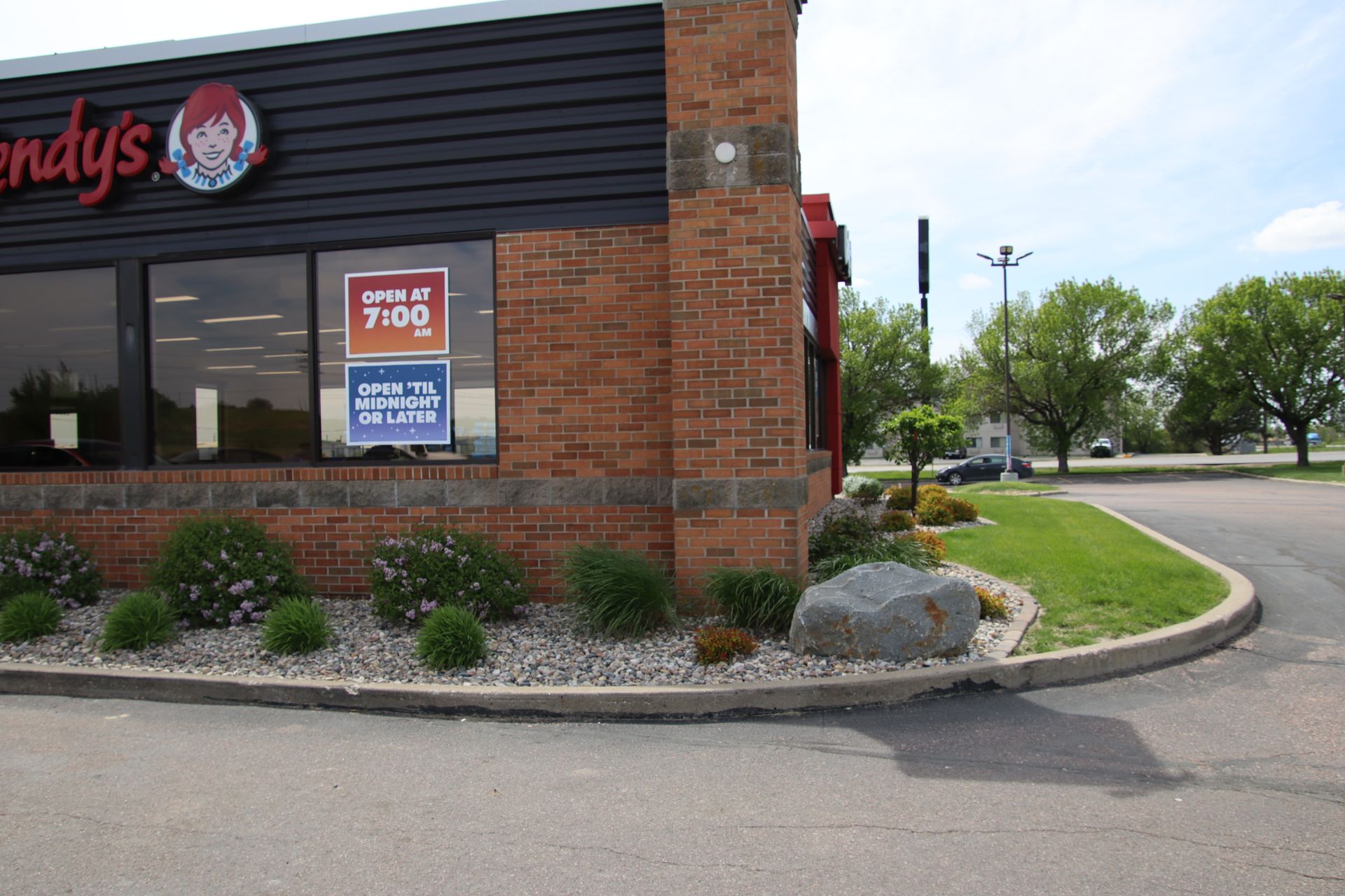 Wendy’s storefront with brick exterior, shrubs, and parking lot on a sunny day