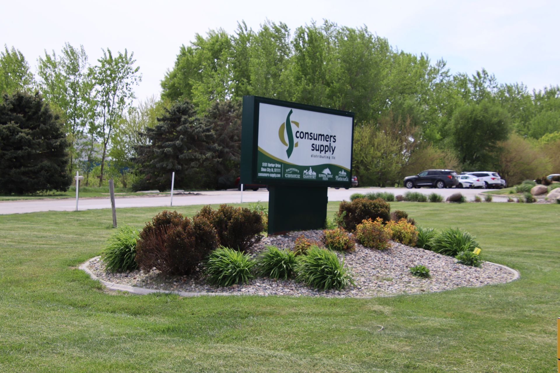 A landscaped sign for a company in front of a grassy area and trees beside a road