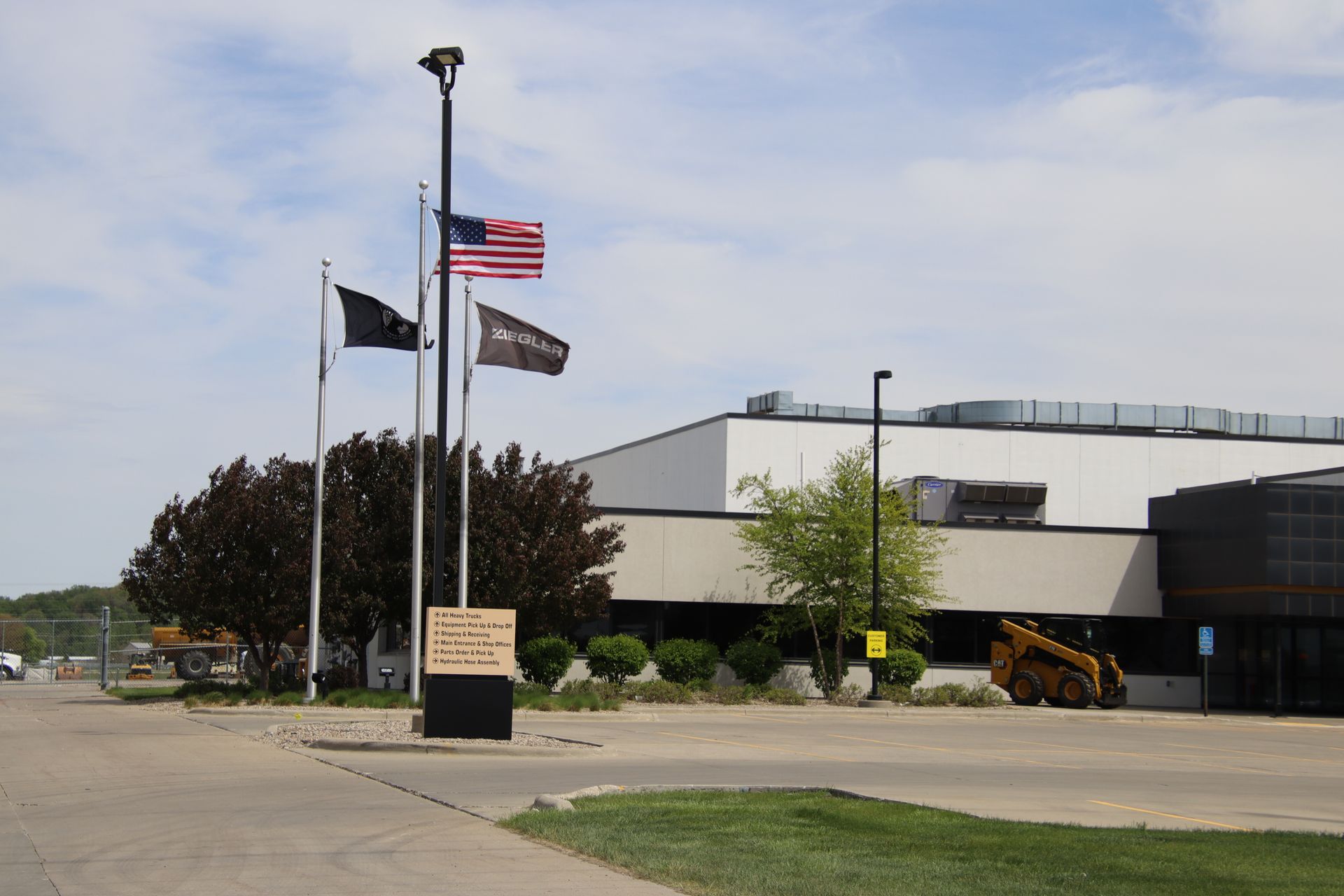 Flagpoles outside a modern building with U.S. and black flags, under a partly cloudy sky.