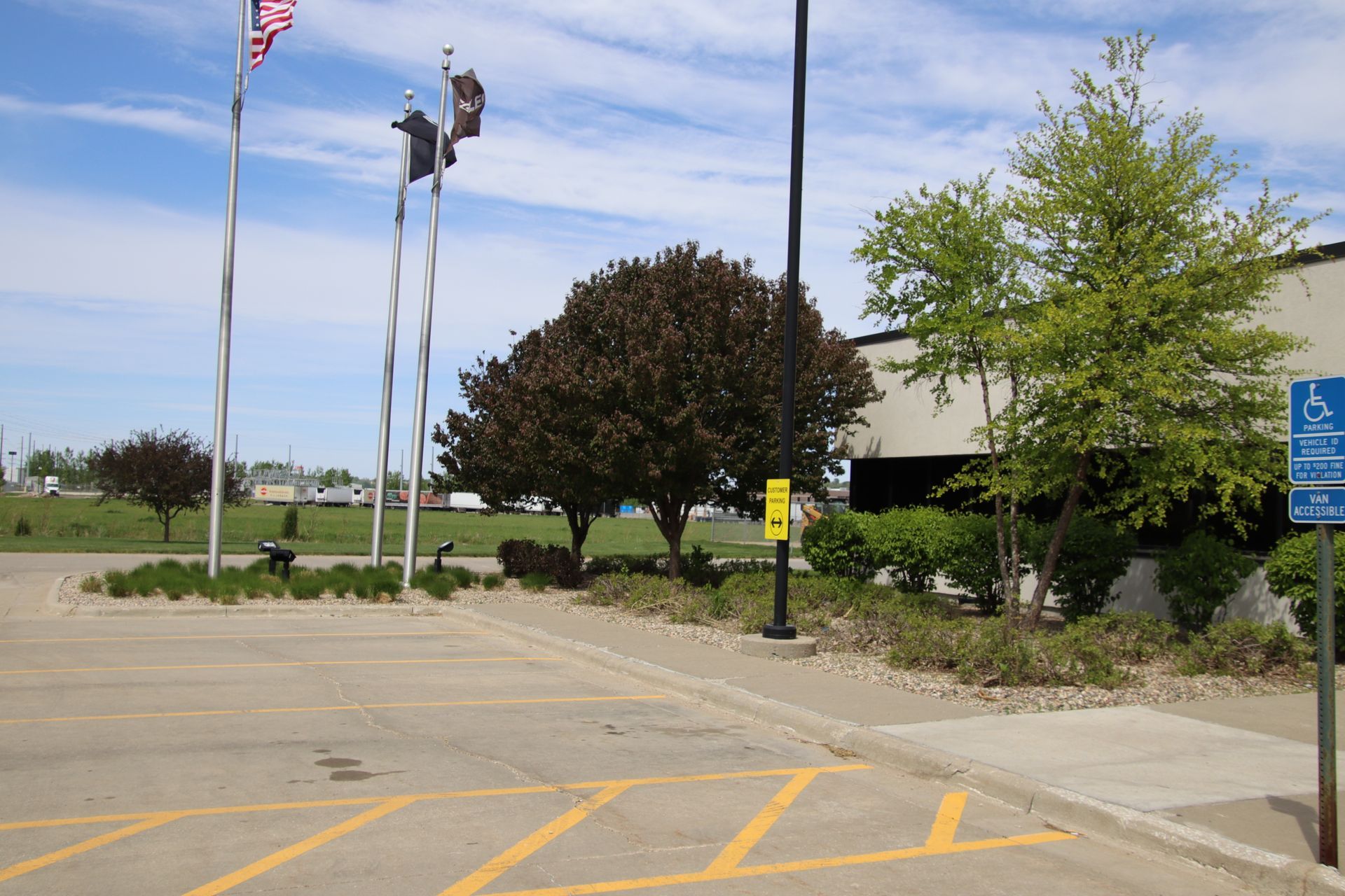Parking lot entrance with flags, trees, and a blue handicapped parking sign