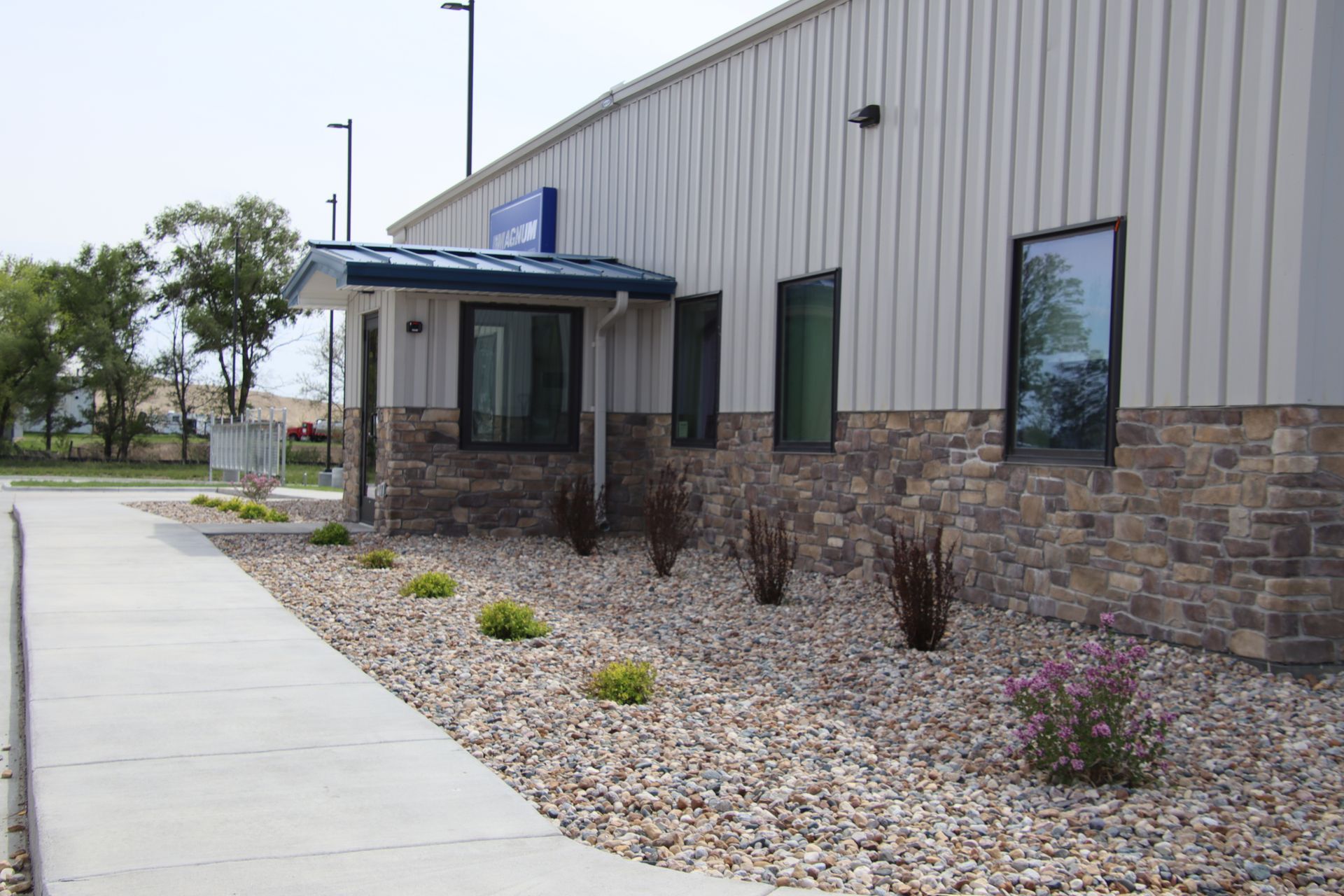 Building entrance with a small covered walkway, stone base, and gravel landscaping beside a concrete sidewalk