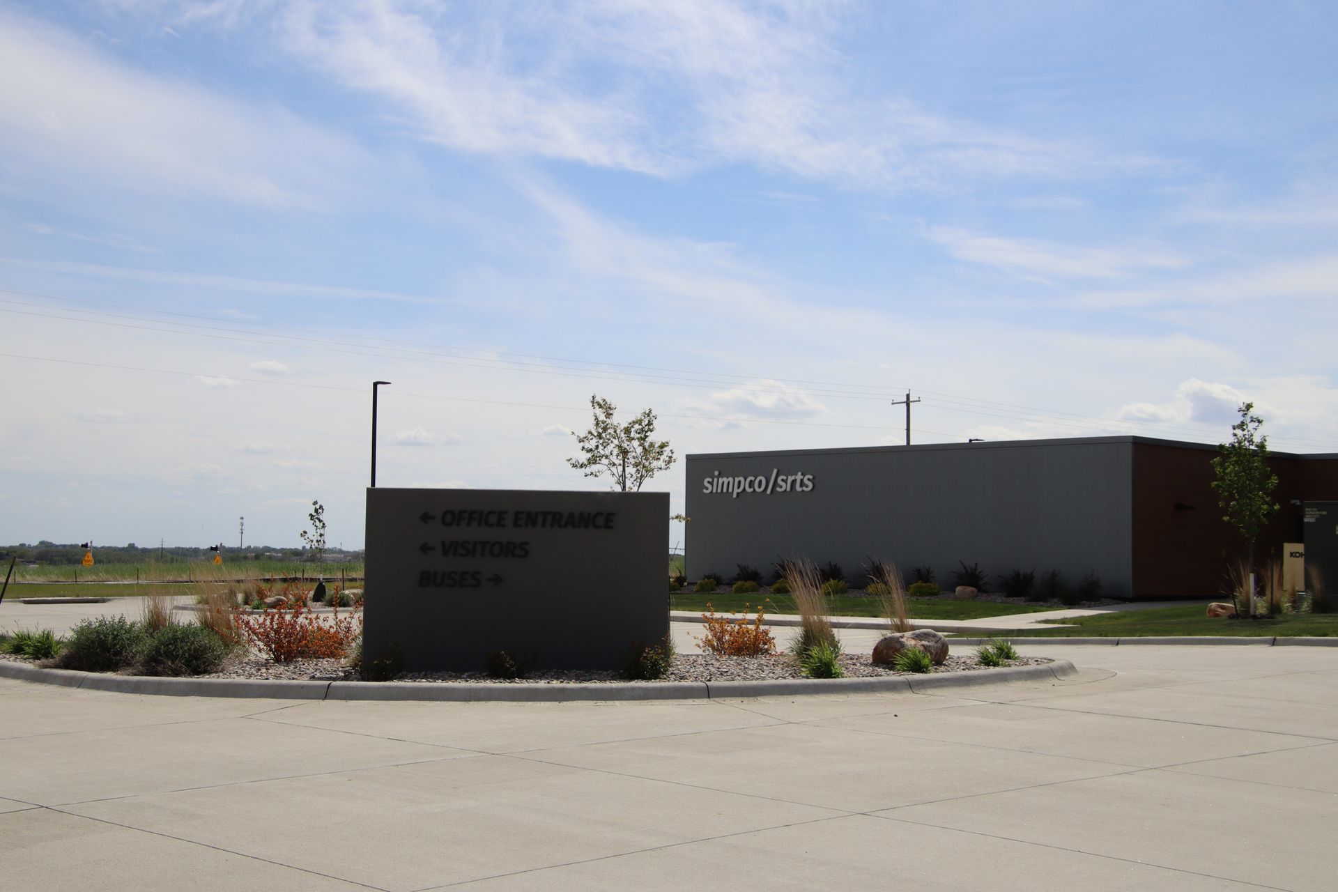 Modern building with a dark sign in a sunny parking lot, under a blue sky