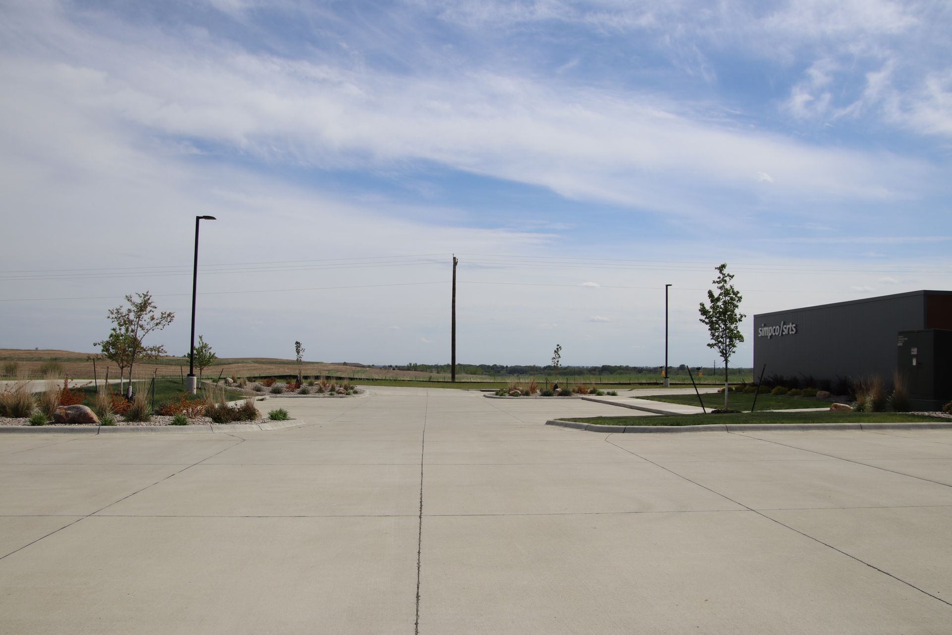 Empty parking lot with concrete pavement, a few lampposts, and a cloudy sky.