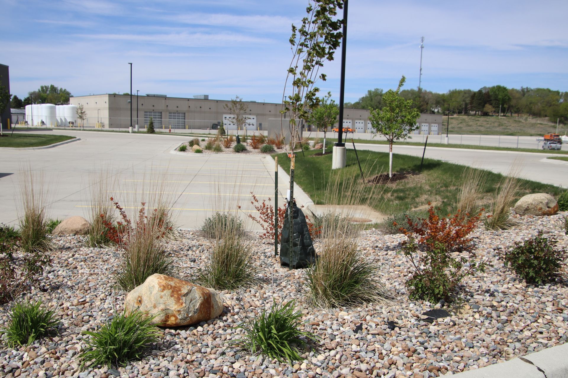 Landscaped parking lot with rocks, small trees, and a beige industrial building in the background