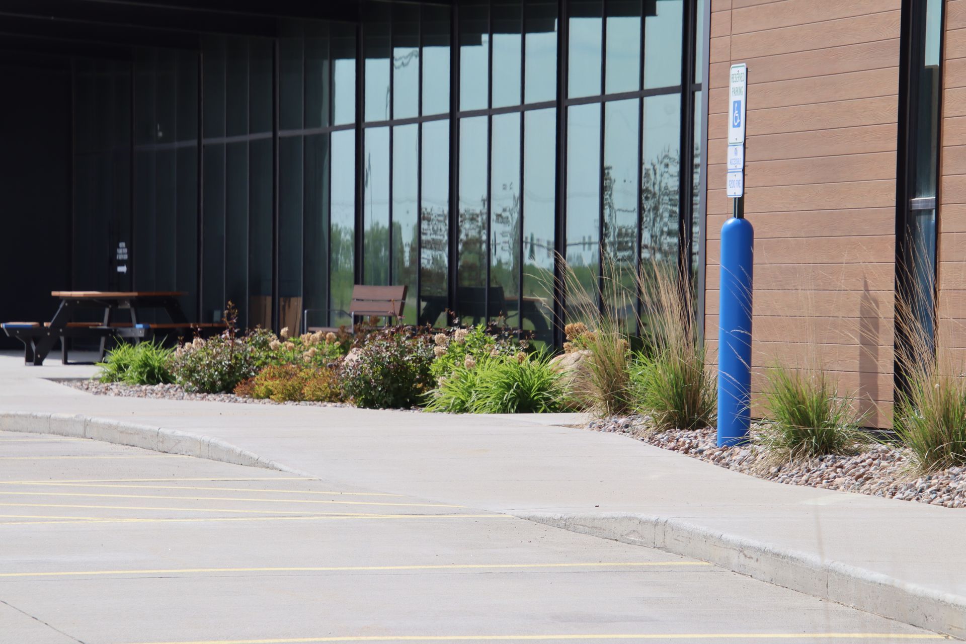 Building entrance with large windows, landscaped shrubs, and a blue bollard by the sidewalk