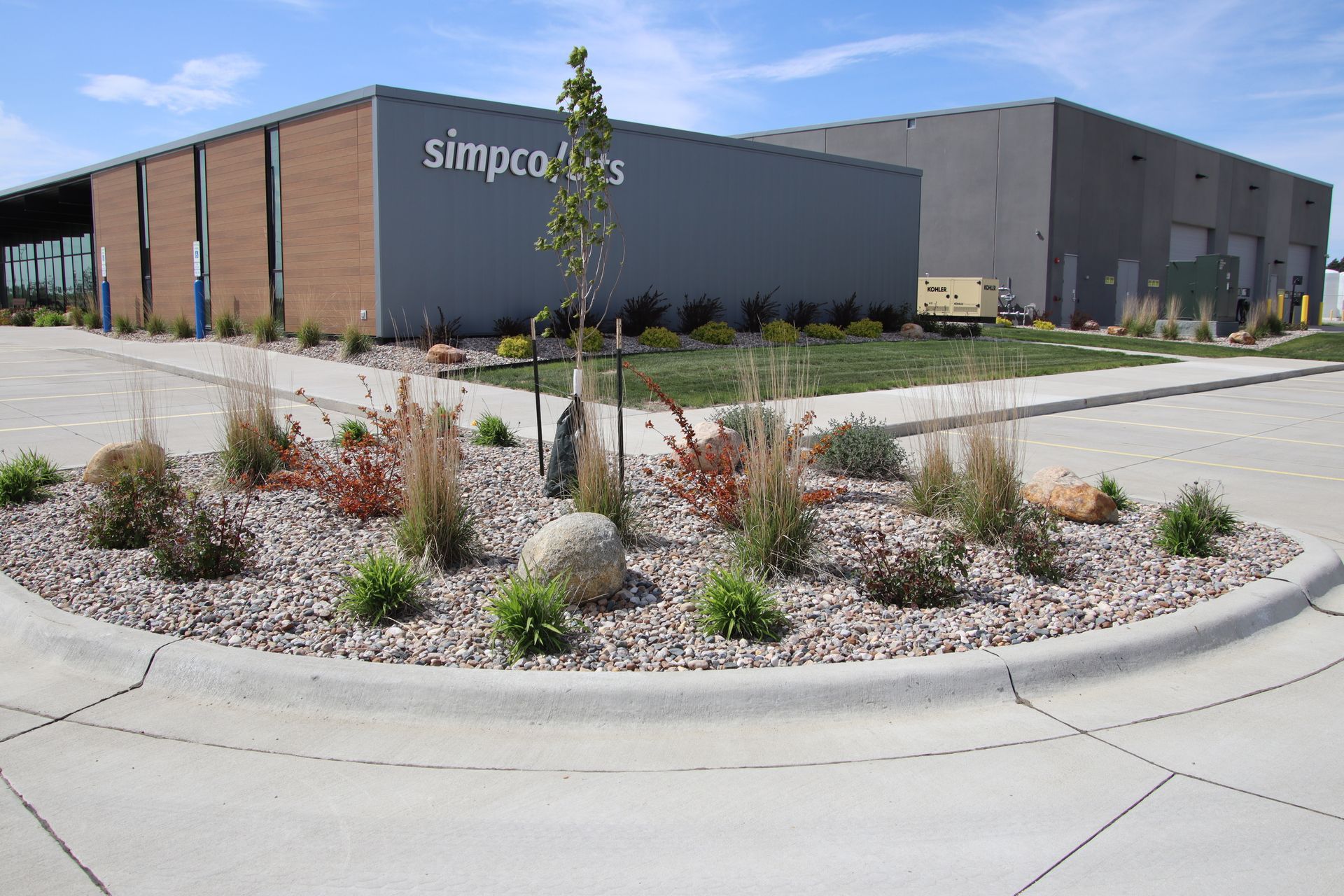 Industrial warehouse building with gray walls, landscaping, and a curved concrete road in front