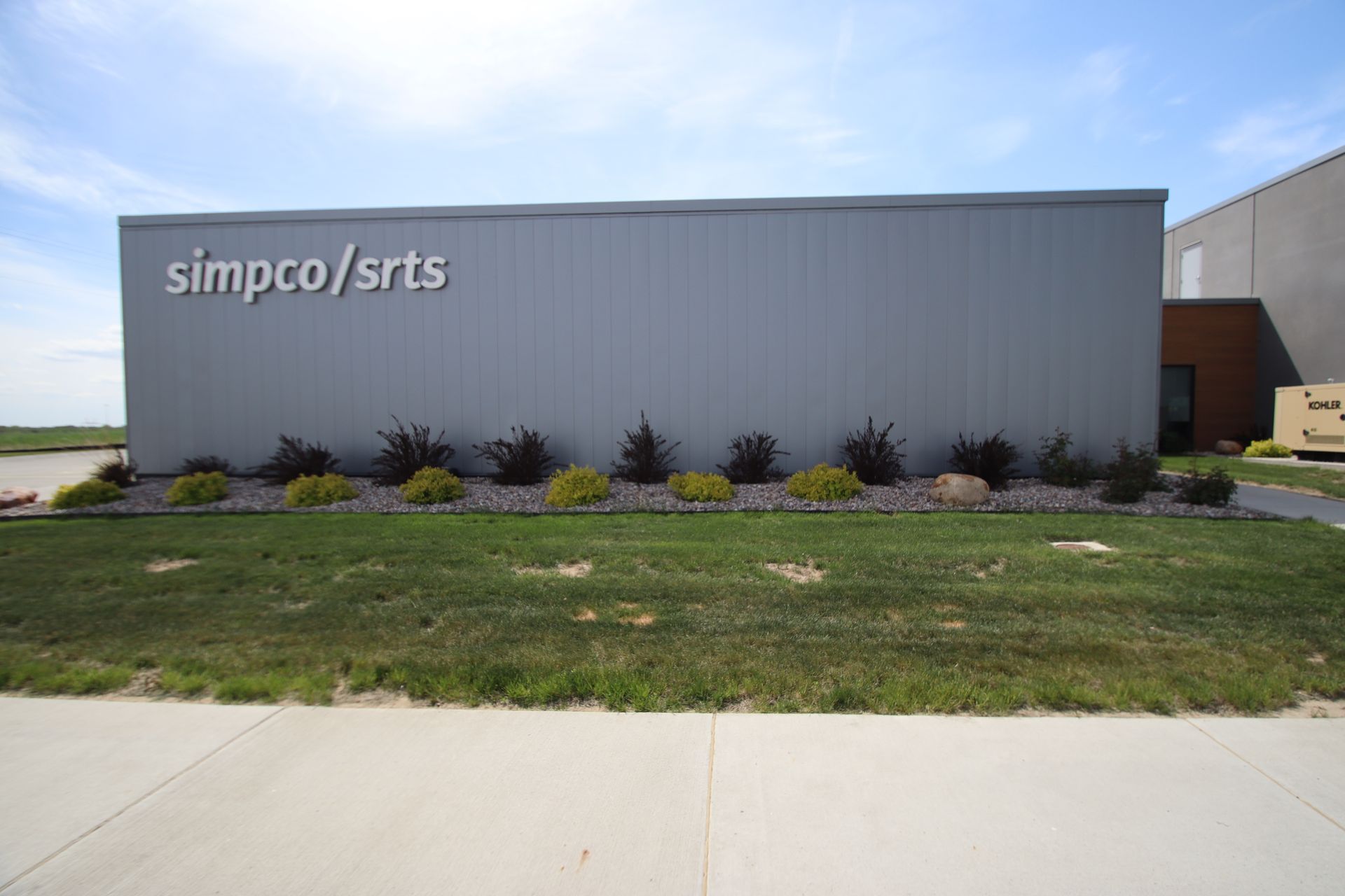 Gray Simpco/SRTS industrial building with small shrubs and a grassy lawn in front