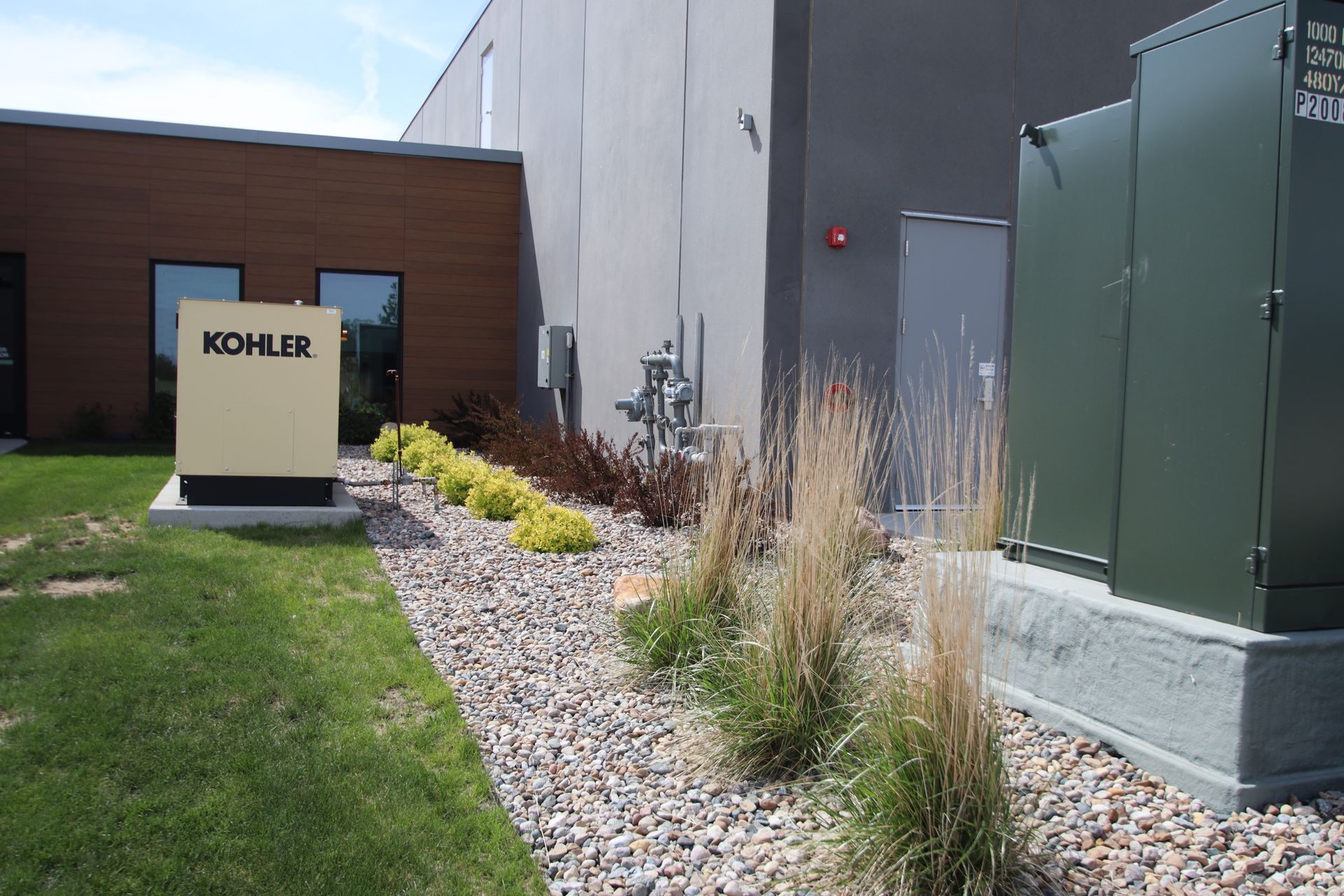 Industrial building exterior with KOHLER sign, grass, gravel landscaping, and electrical units