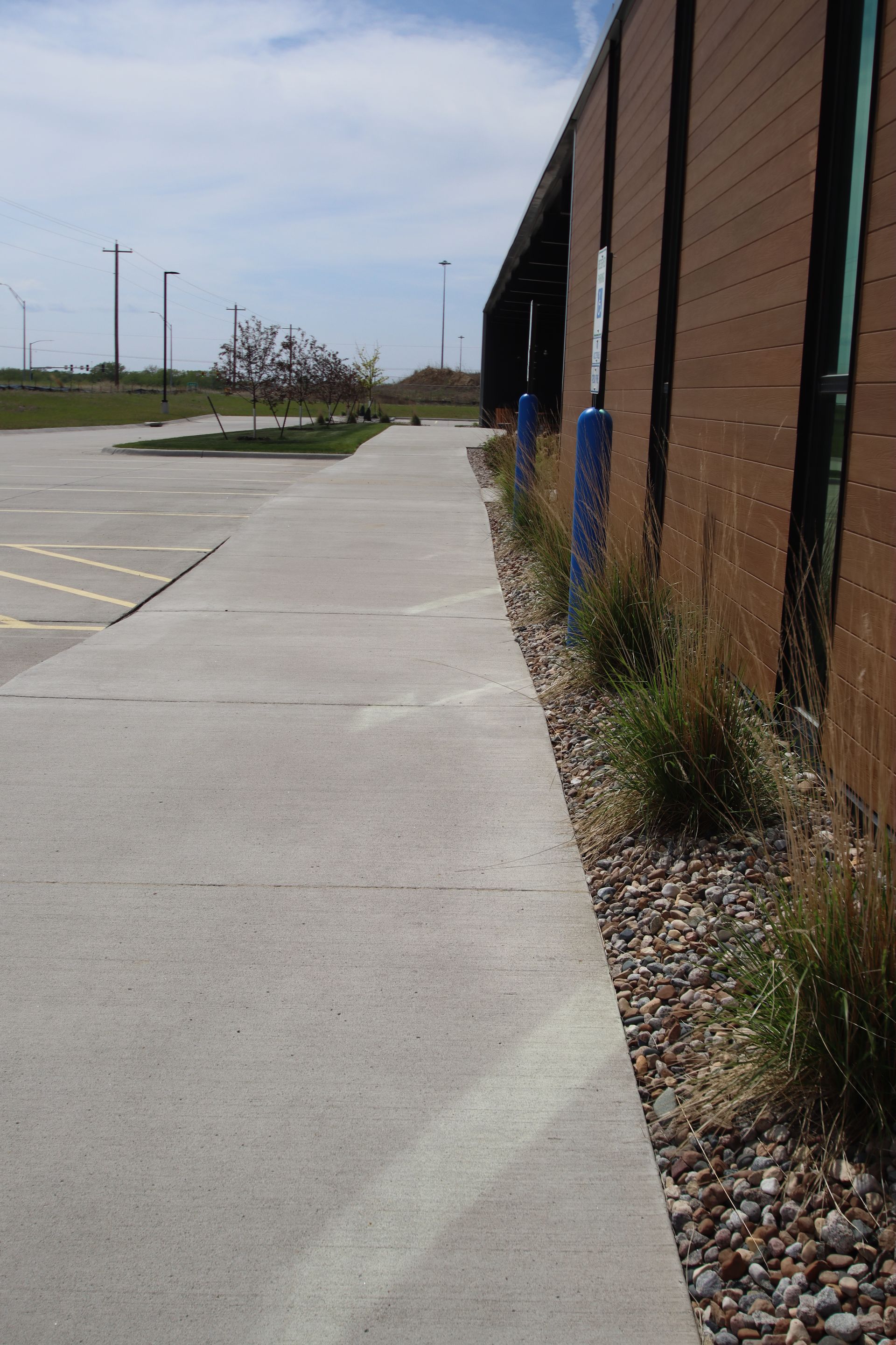 Sidewalk beside a brick building with gravel landscaping and blue posts under a clear sky