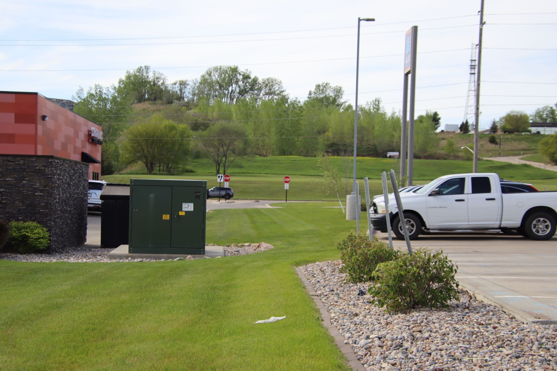 White pickup parked beside a grassy roadside with utility boxes and a gravel bed under cloudy skies