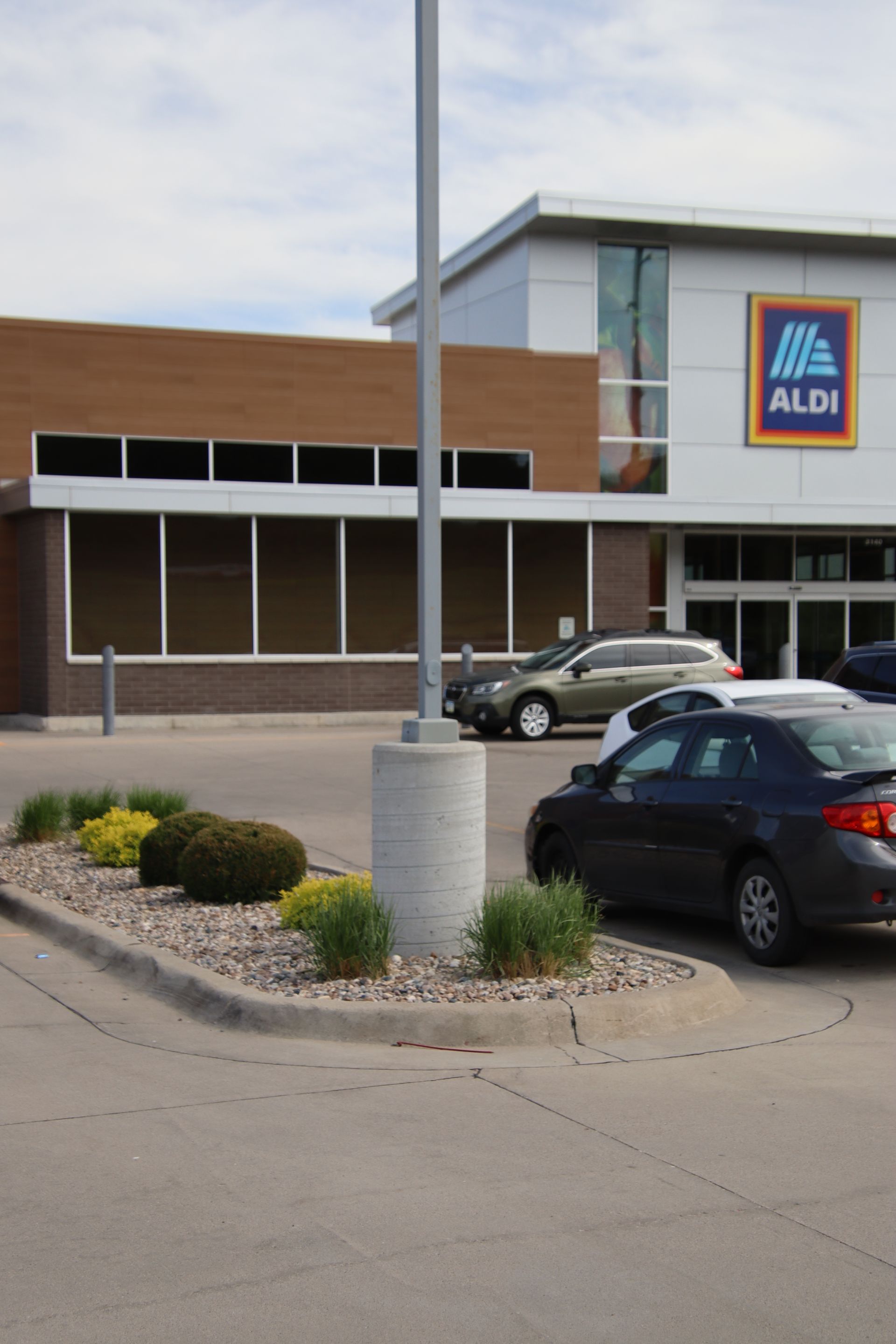 ALDI store entrance with parked cars and a landscaped lot under a cloudy sky
