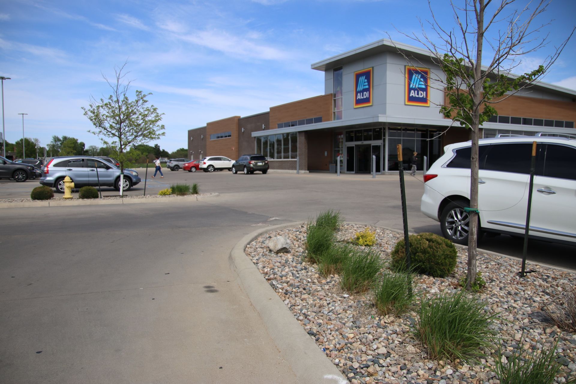 Parking lot in front of a storefront, with parked cars, desert landscaping, and a clear blue sky.