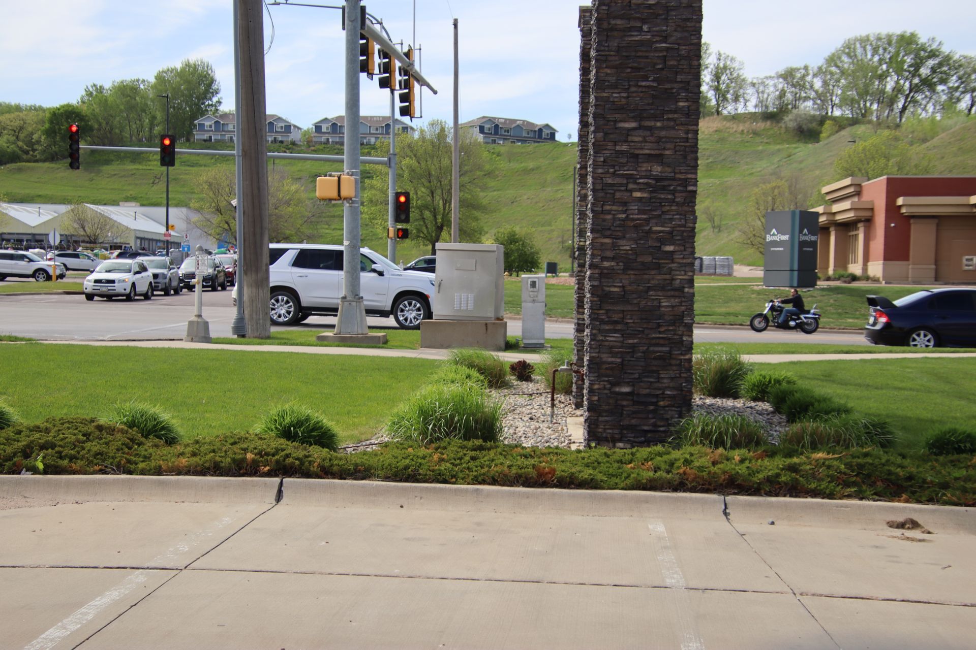 Roadside intersection with a silver SUV, traffic lights, and a motorcycle near a brick building.