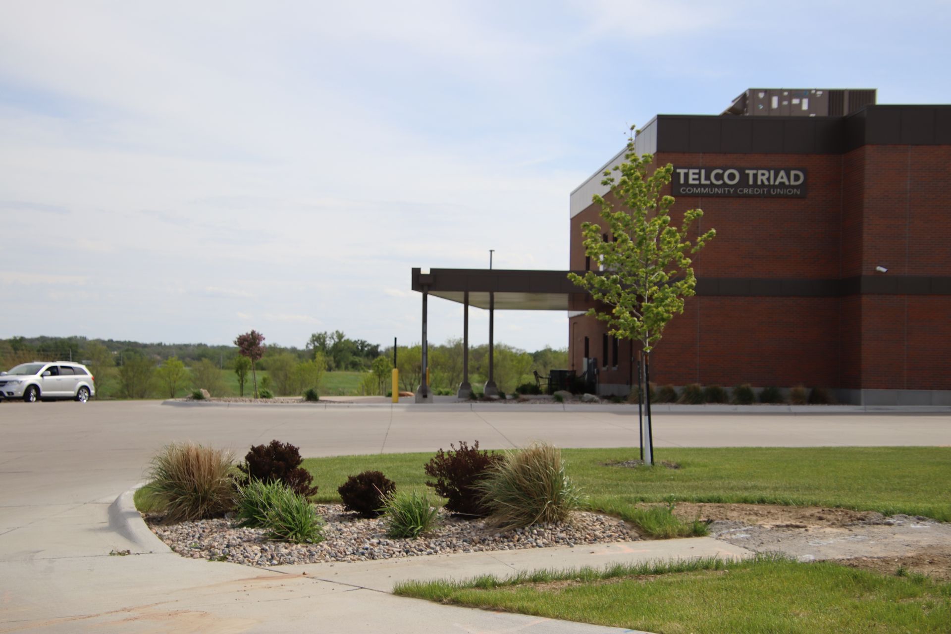 Teleo Tmad building with parking lot, landscaped shrubs, and a white car under a partly cloudy sky