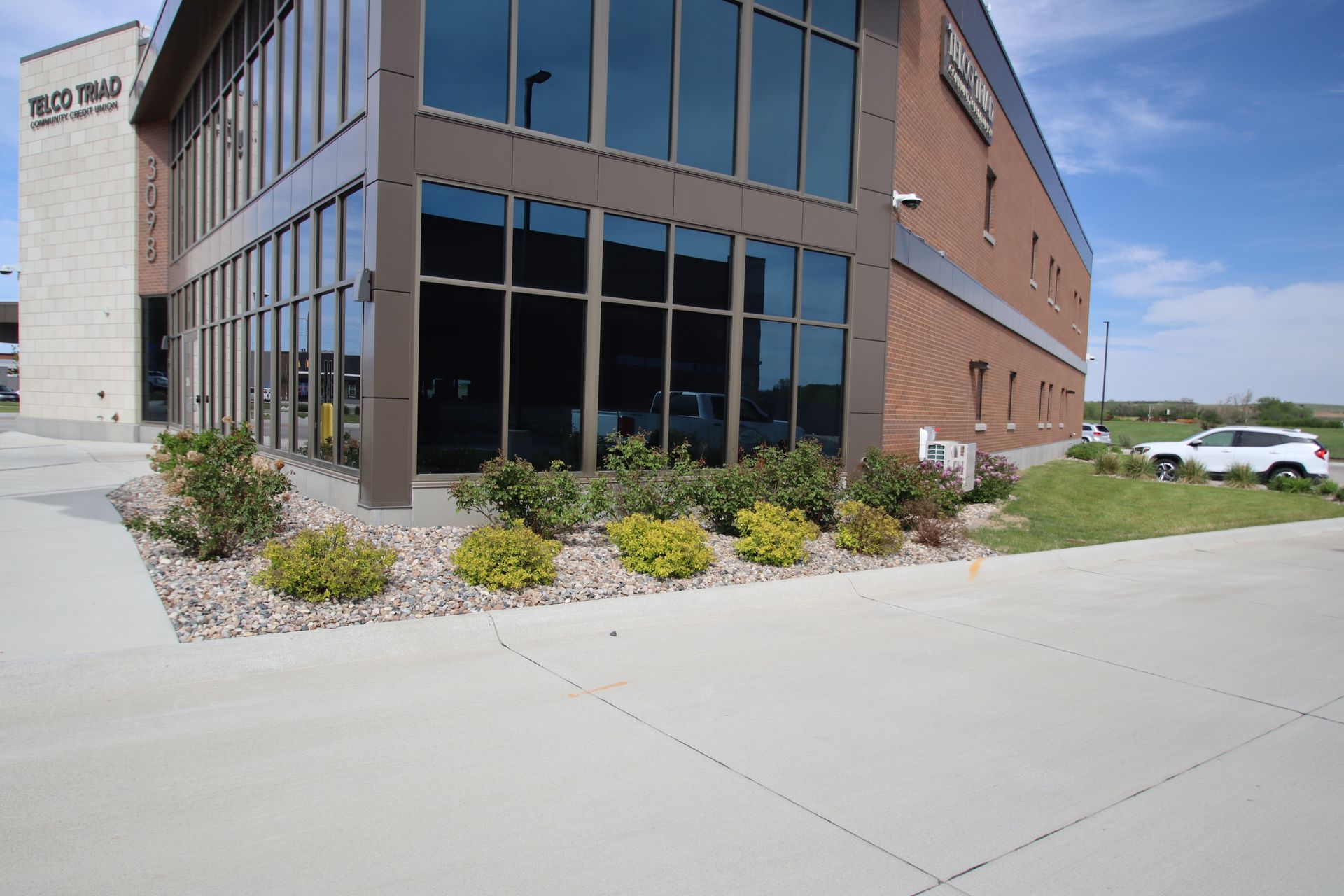 Modern brick office building with large windows, landscaping, and a sidewalk on a clear day