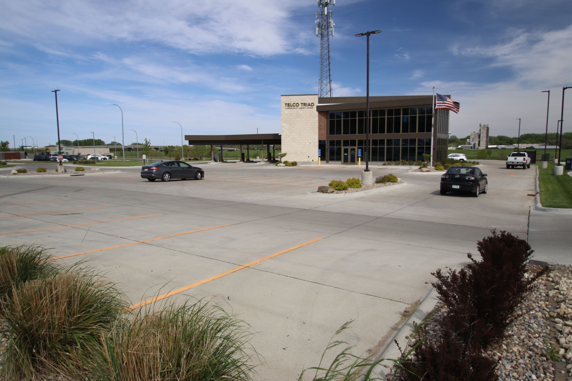 Parking lot with two cars near a modern building and cell tower under a clear sky