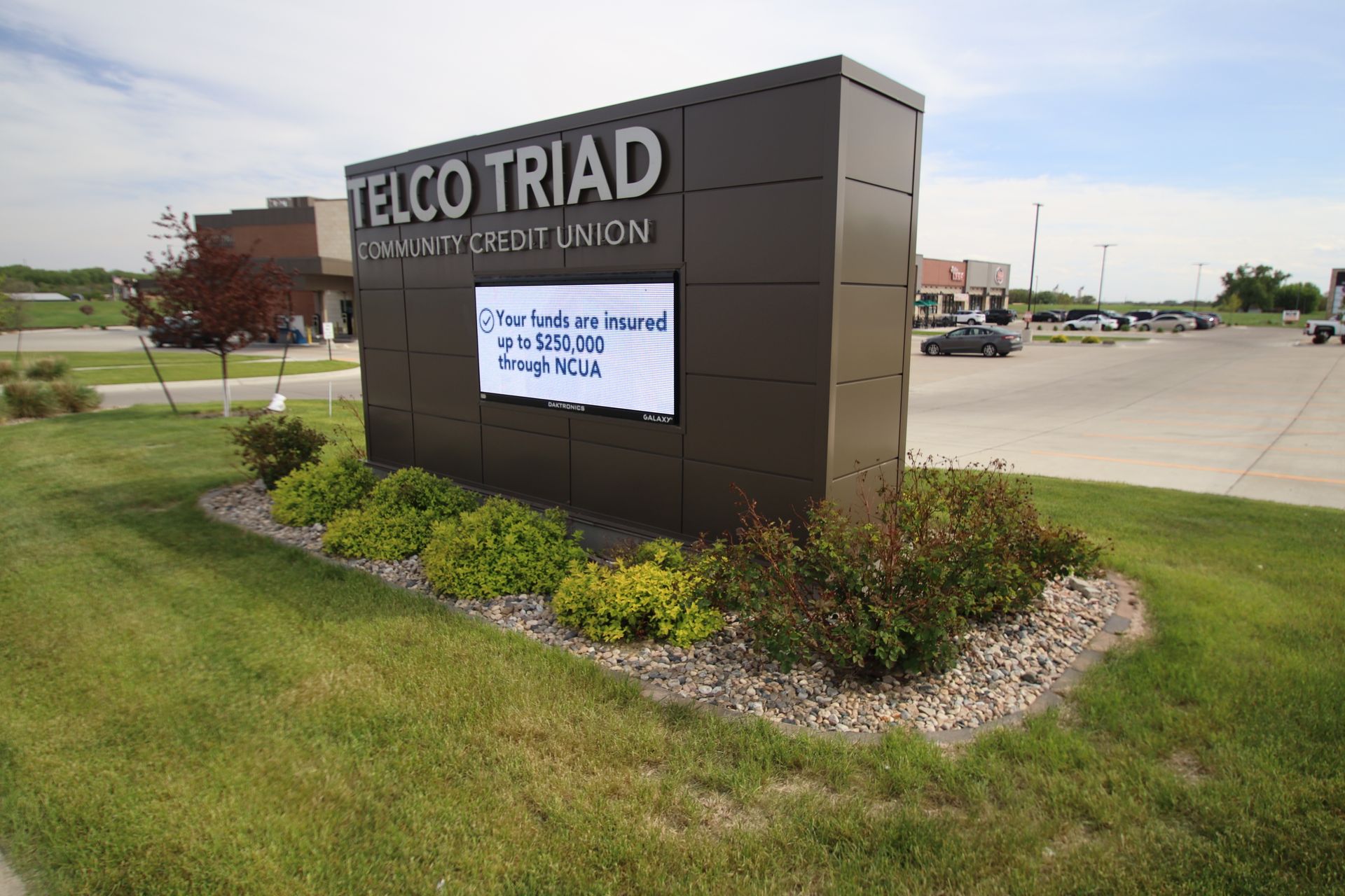 TELCO TRIAD sign in a landscaped roadside area with a digital display board