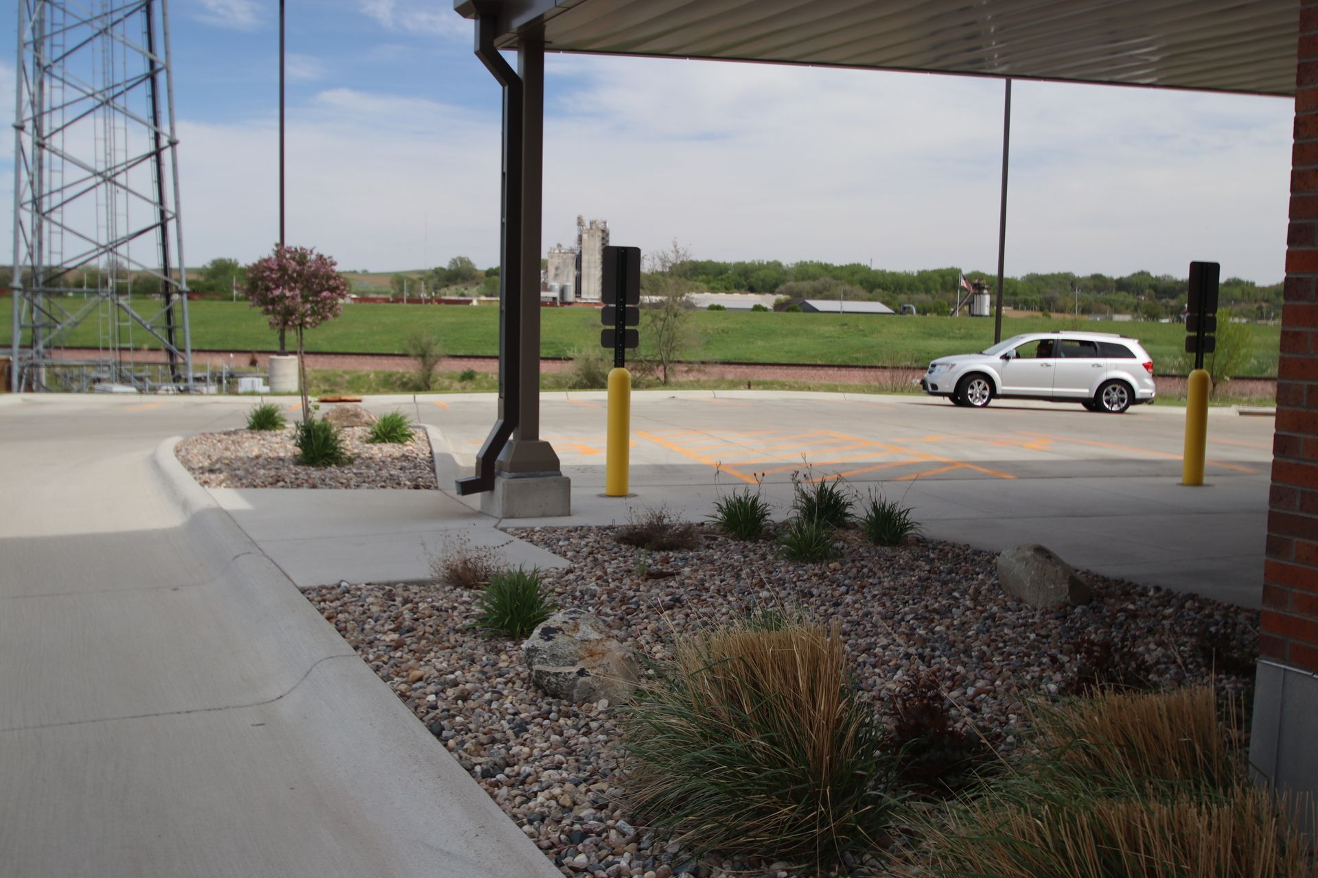 Covered driveway beside landscaped parking lot with a white car in the distance
