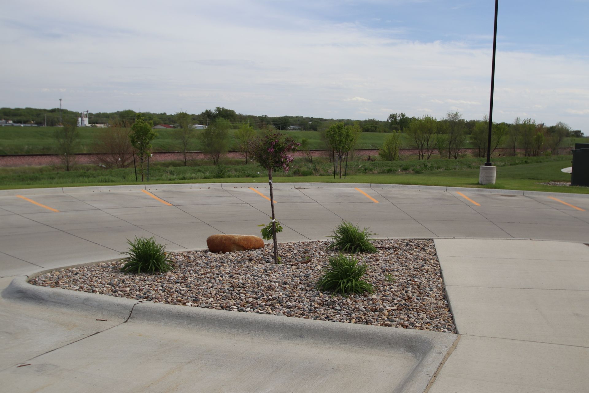 Desert-style traffic island with rocks and small shrubs beside a paved road under an overcast sky