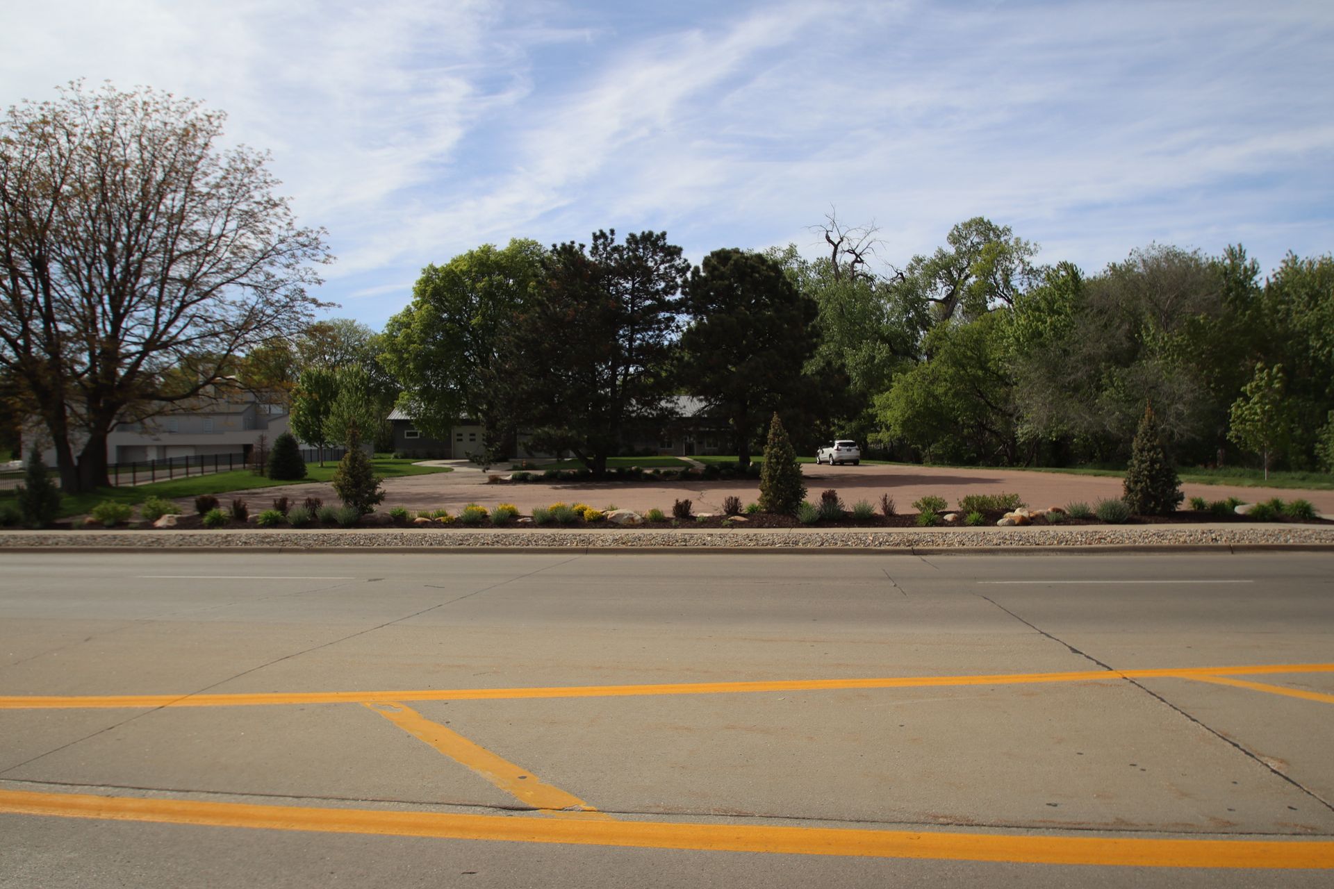 Wide road with yellow markings in front of a tree-lined landscaped median under a cloudy sky