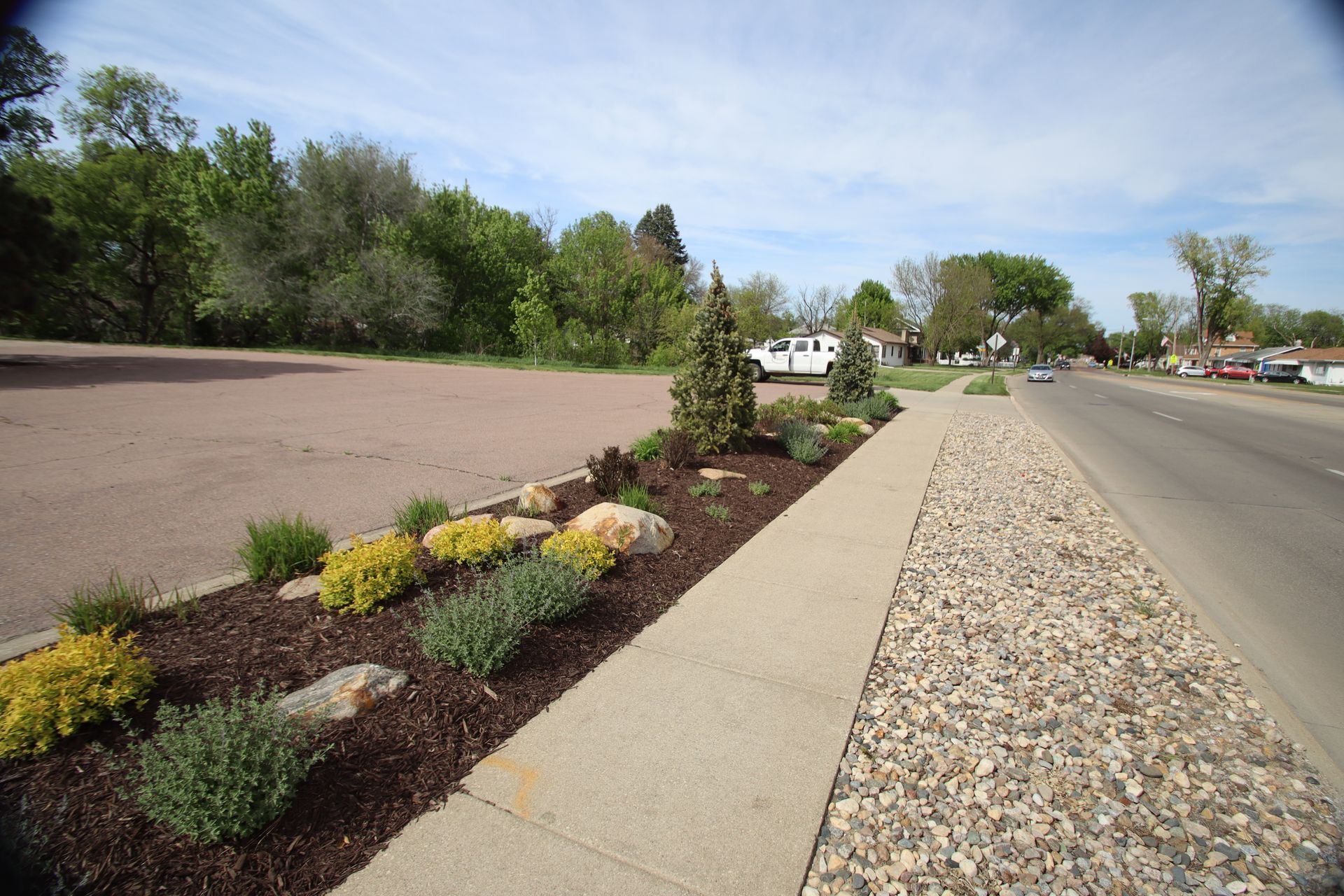 Landscaped roadside with gravel median, sidewalk, and young shrubs under a clear sky