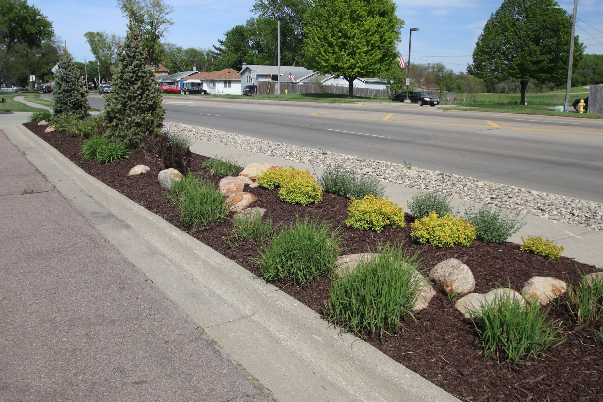 Landscaped roadside flower bed with rocks and shrubs beside a paved street