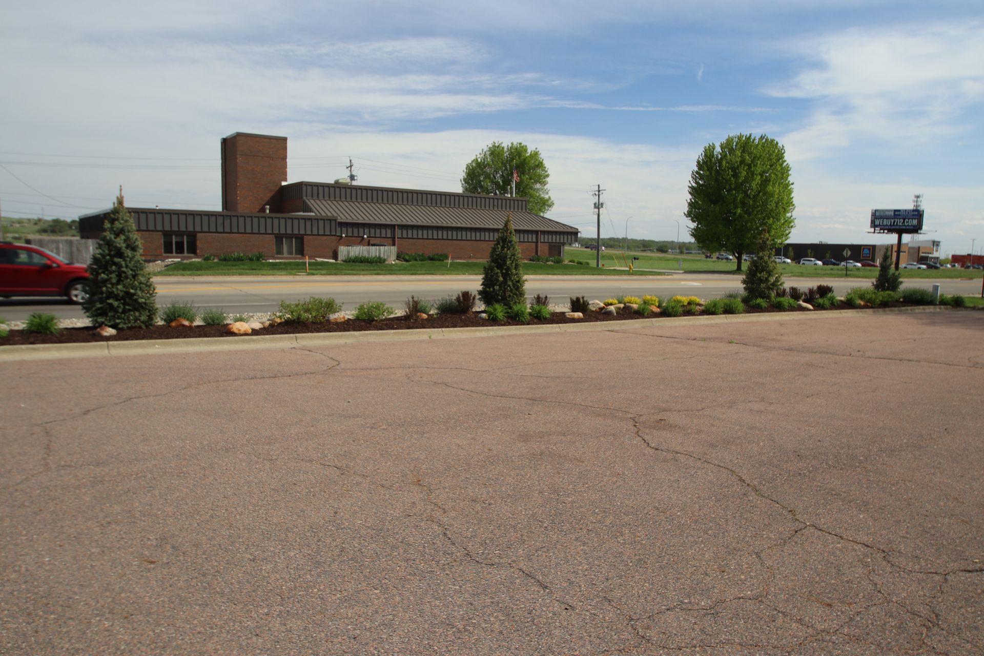 Empty parking lot beside a low brick building and trees under a cloudy sky