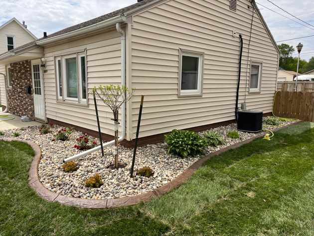 Curved garden border beside a house with fresh soil and sod in a green yard.