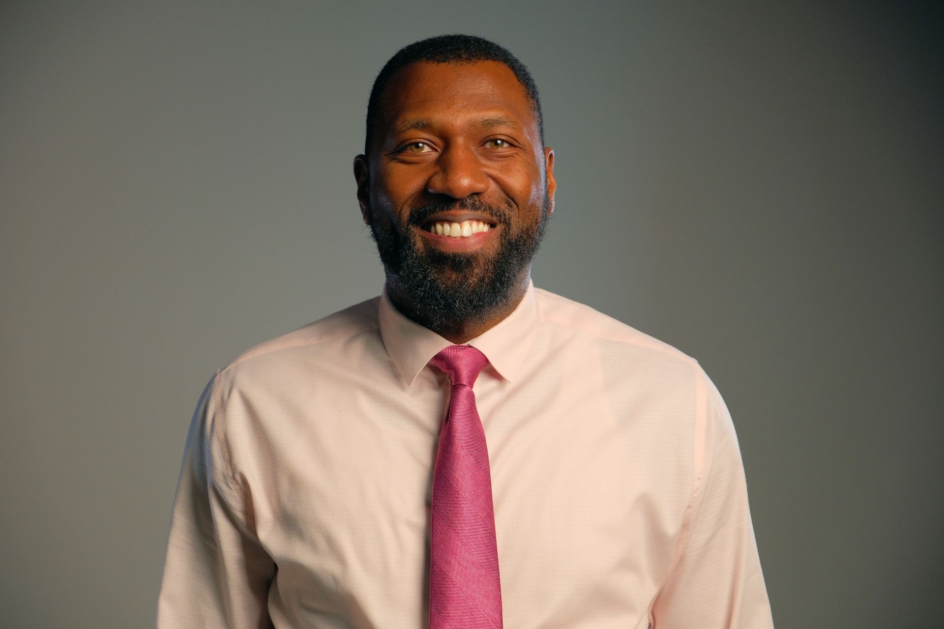 Smiling man in a white shirt and pink tie against a gray background
