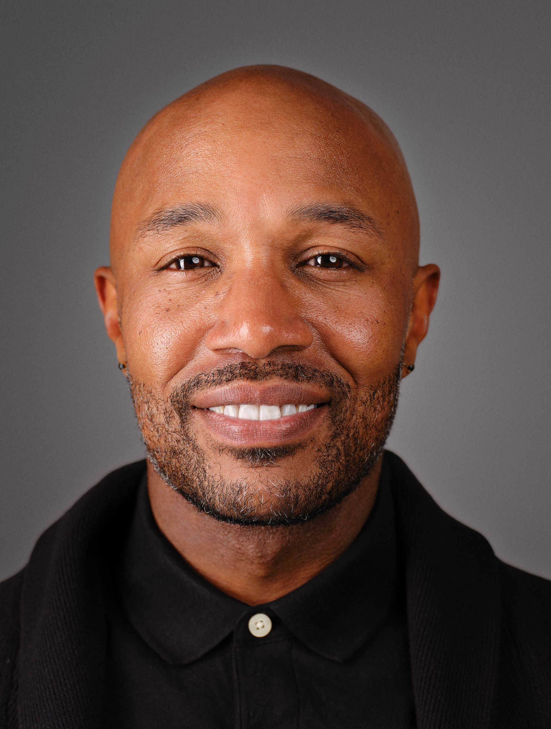 Portrait of a smiling man in a black shirt against a gray background