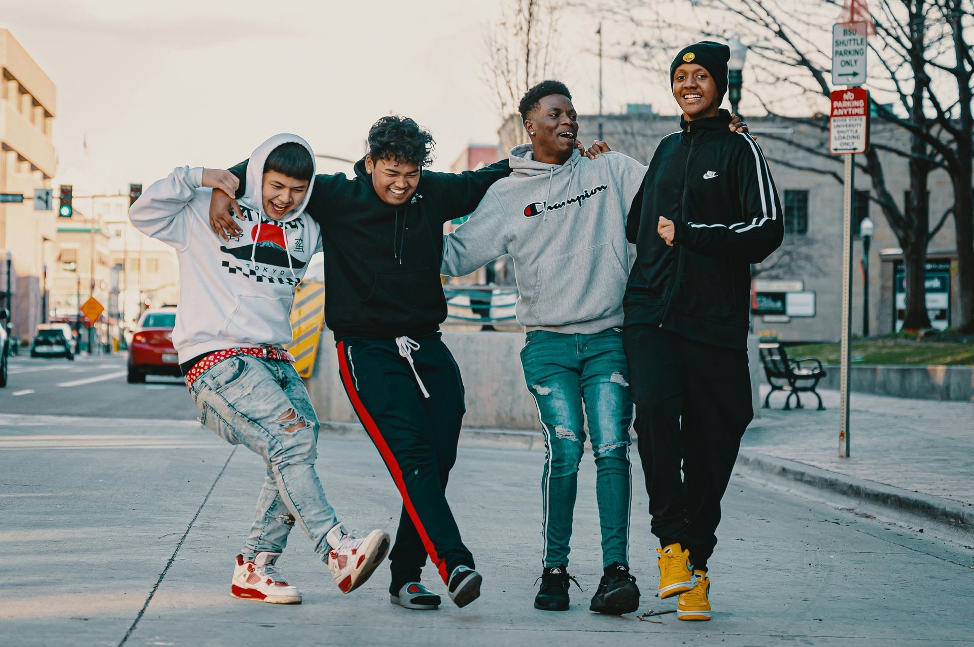 Four friends walking arm-in-arm on a city street, smiling in casual clothes.