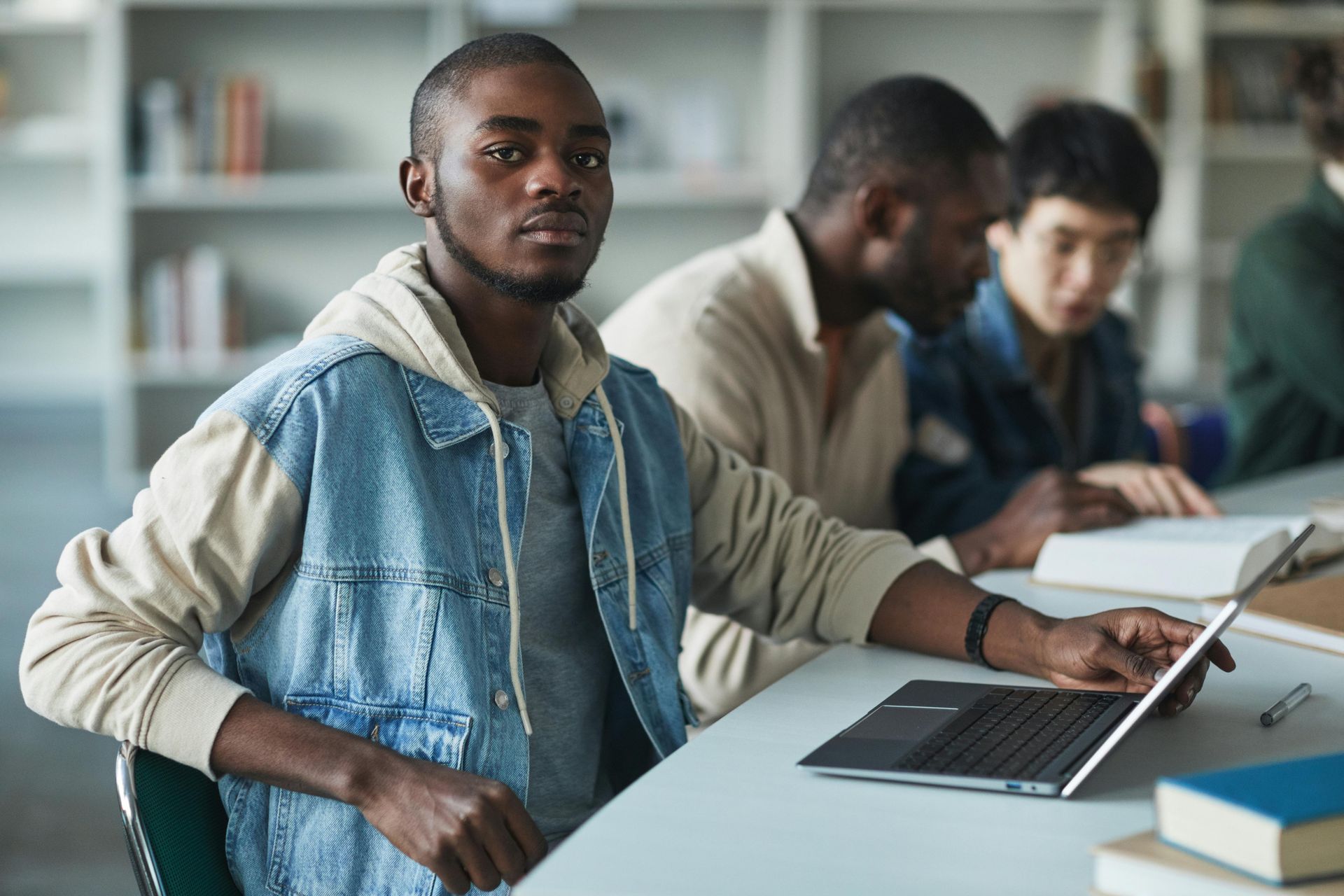 Student working on a laptop in a classroom, with two others studying in the background.
