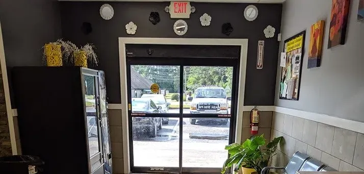 Small storefront interior with glass doors, black walls, tiled counter, and plants near the entrance