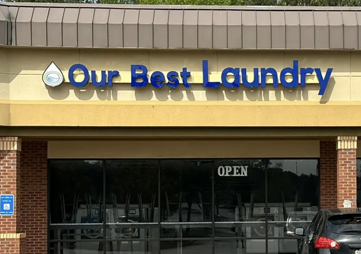 Storefront sign for “Our Best Laundry” above a laundromat entrance with an “OPEN” sign