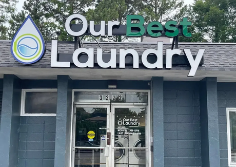 Storefront sign for Our Best Laundry above glass entrance on a gray building