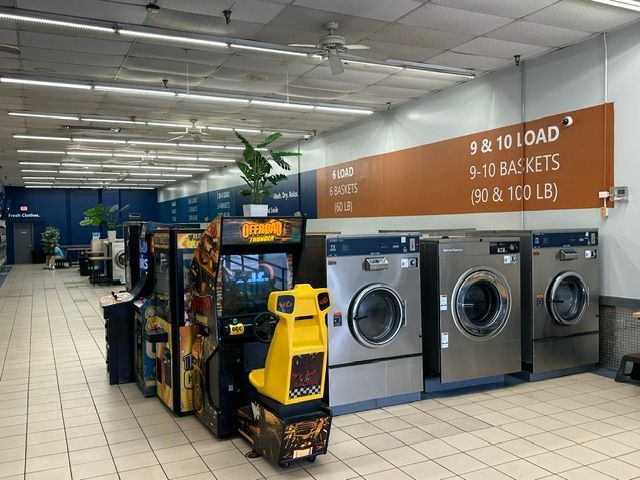 Laundry room with rows of washers and dryers, yellow cart, and orange wall signs for load sizes.